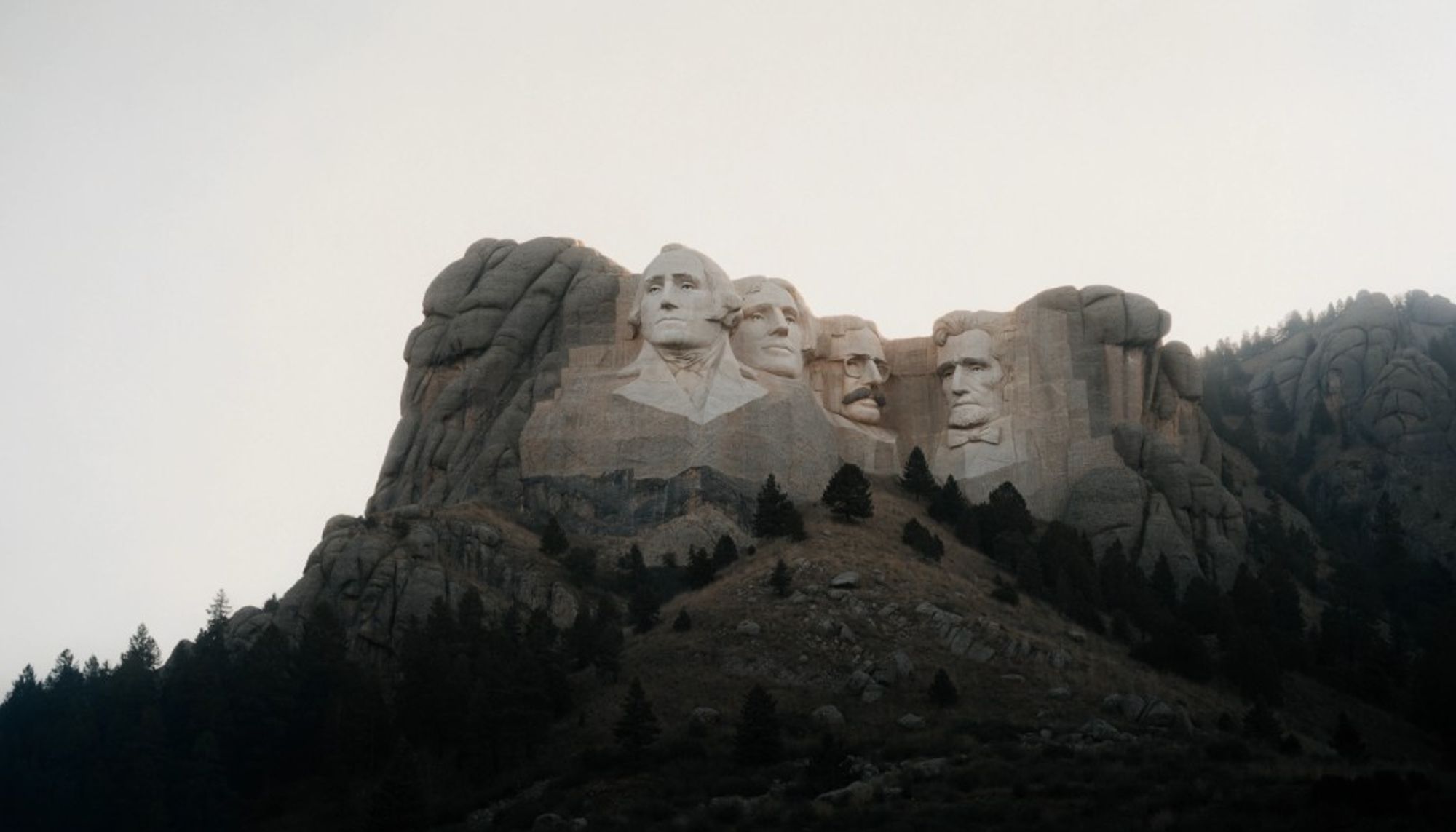 The carved faces of four presidents on a granite mountain above a pine forest