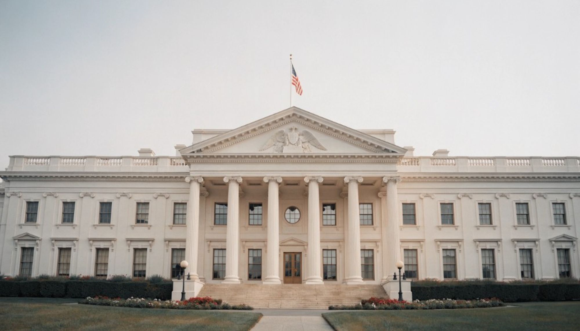 The north front of the White House, with its columned portico and an American flag on the roof