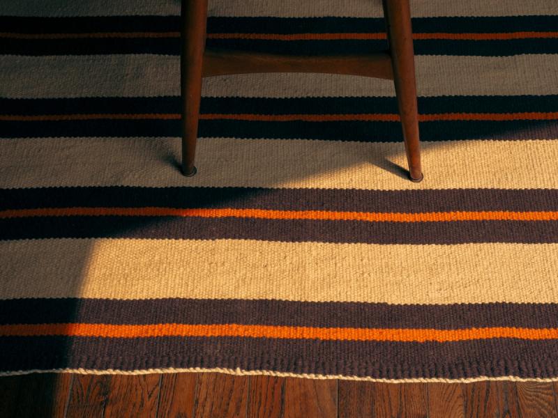 Closeup of striped rug with legs of chair towards top of frame