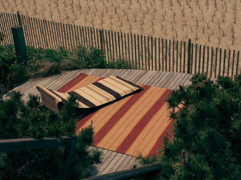 striped rugs on deck with fence and sand