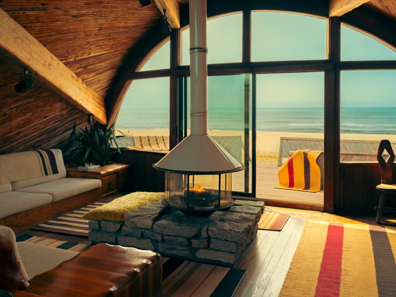 Interior depicting freestanding modern fireplace surrounded by rugs with ocean in background