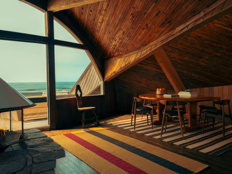 Rugs under table with curved wooden roof and large window with ocean in the background