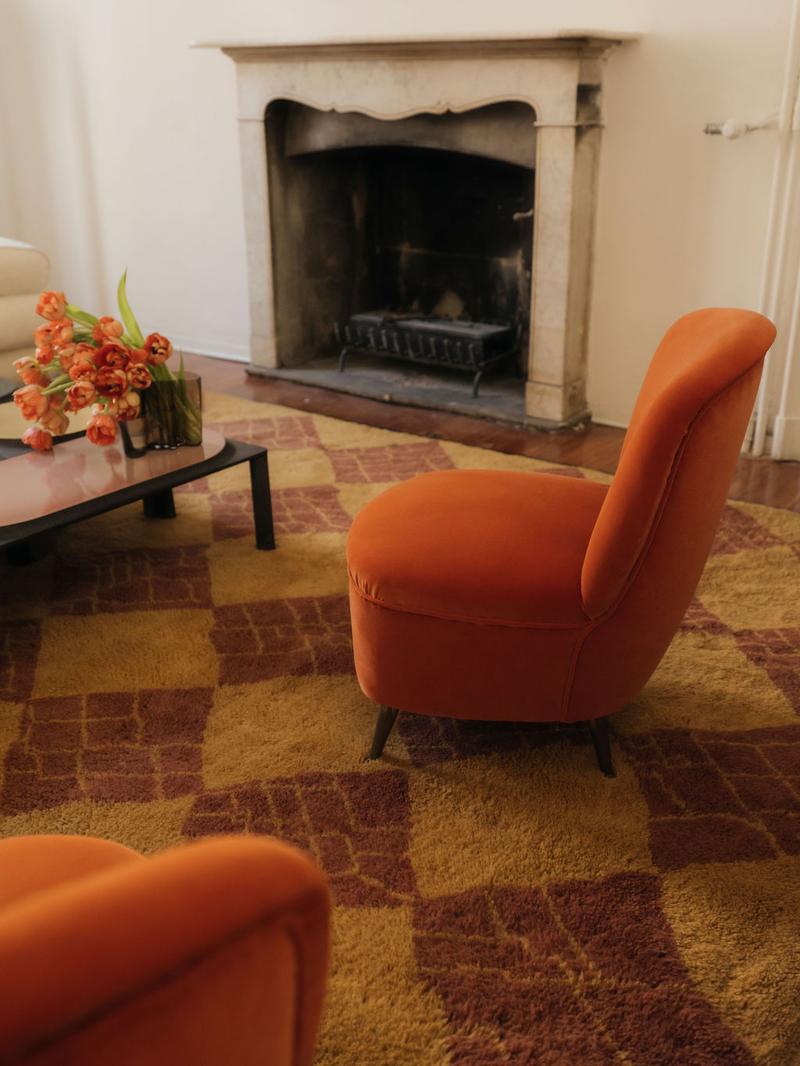 Checkerboard rug in a living room with two orange chairs, black coffee table, and stone fireplace