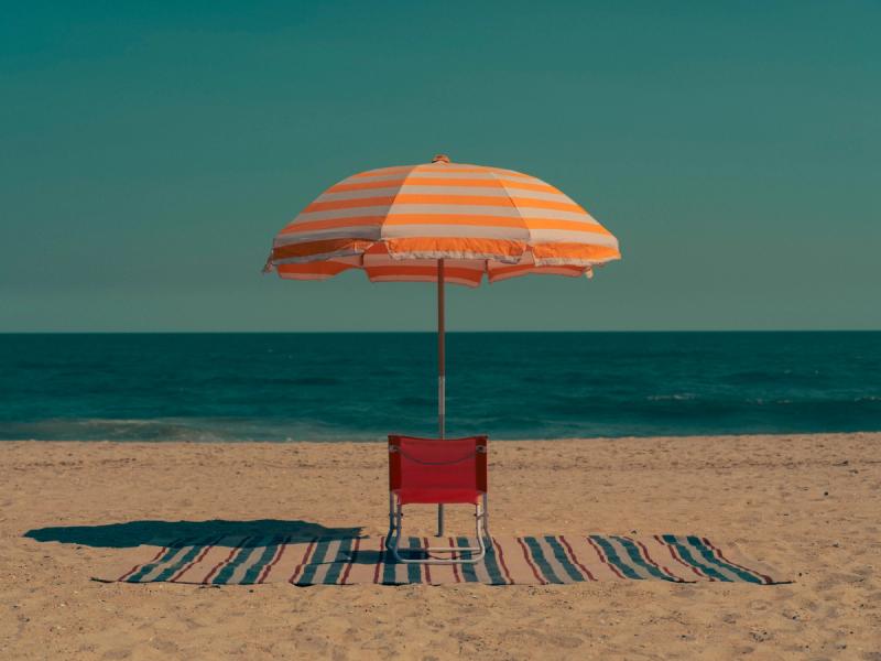 beach, rug, chair on rug, beach umbrella in fron of chair, ocean and sky