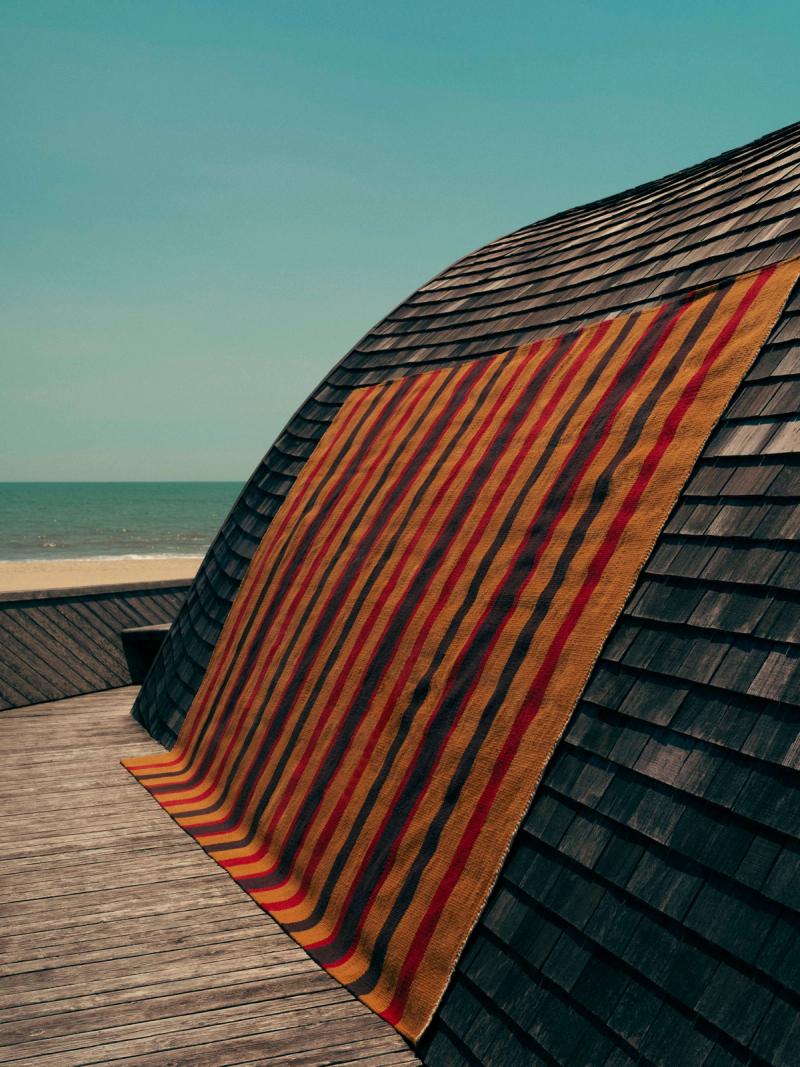 Rug draped on curved wooden roof with ocean in background