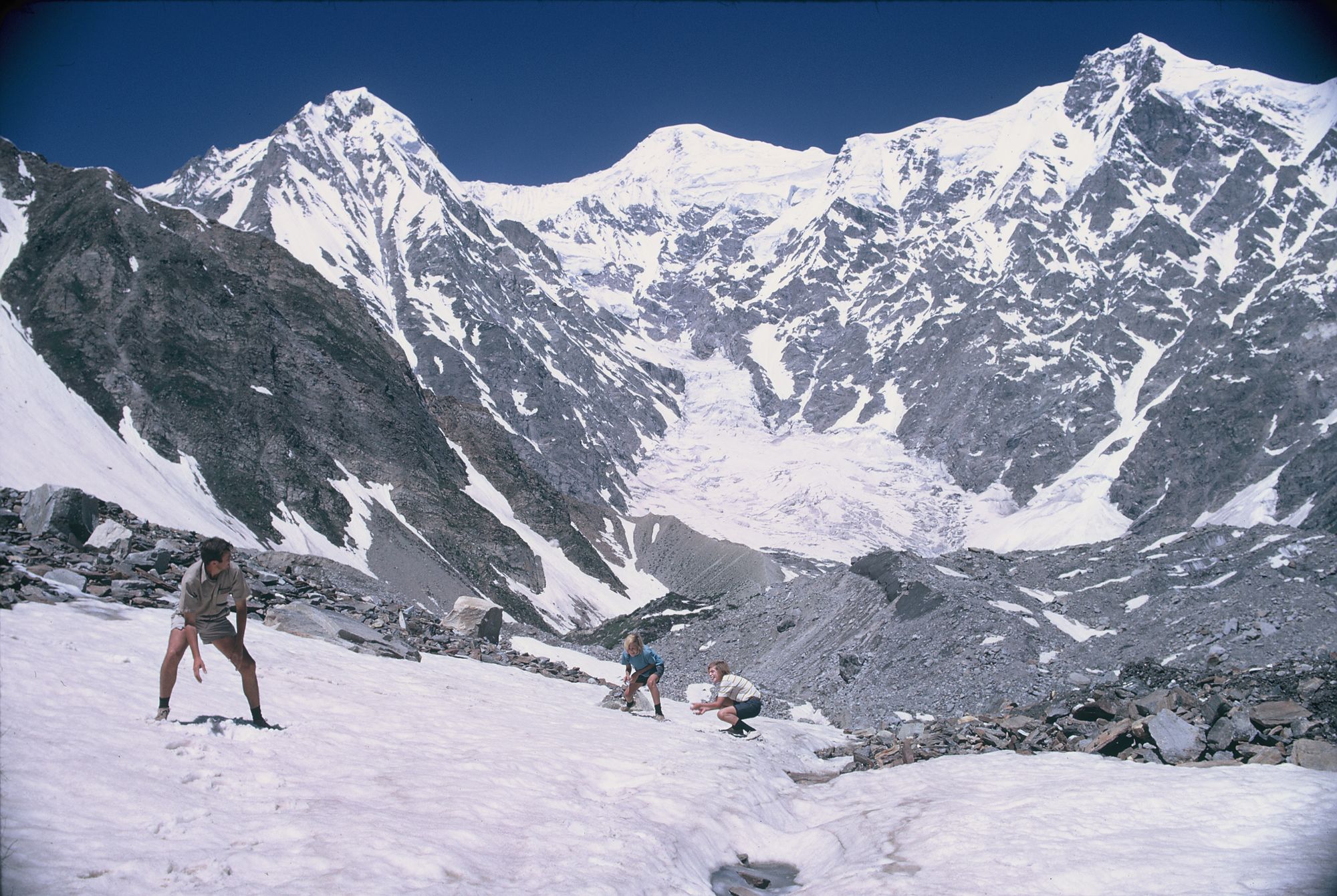 A white man and his two sons photographed mid-snowball fight, at the foot of a dramatic mountain.