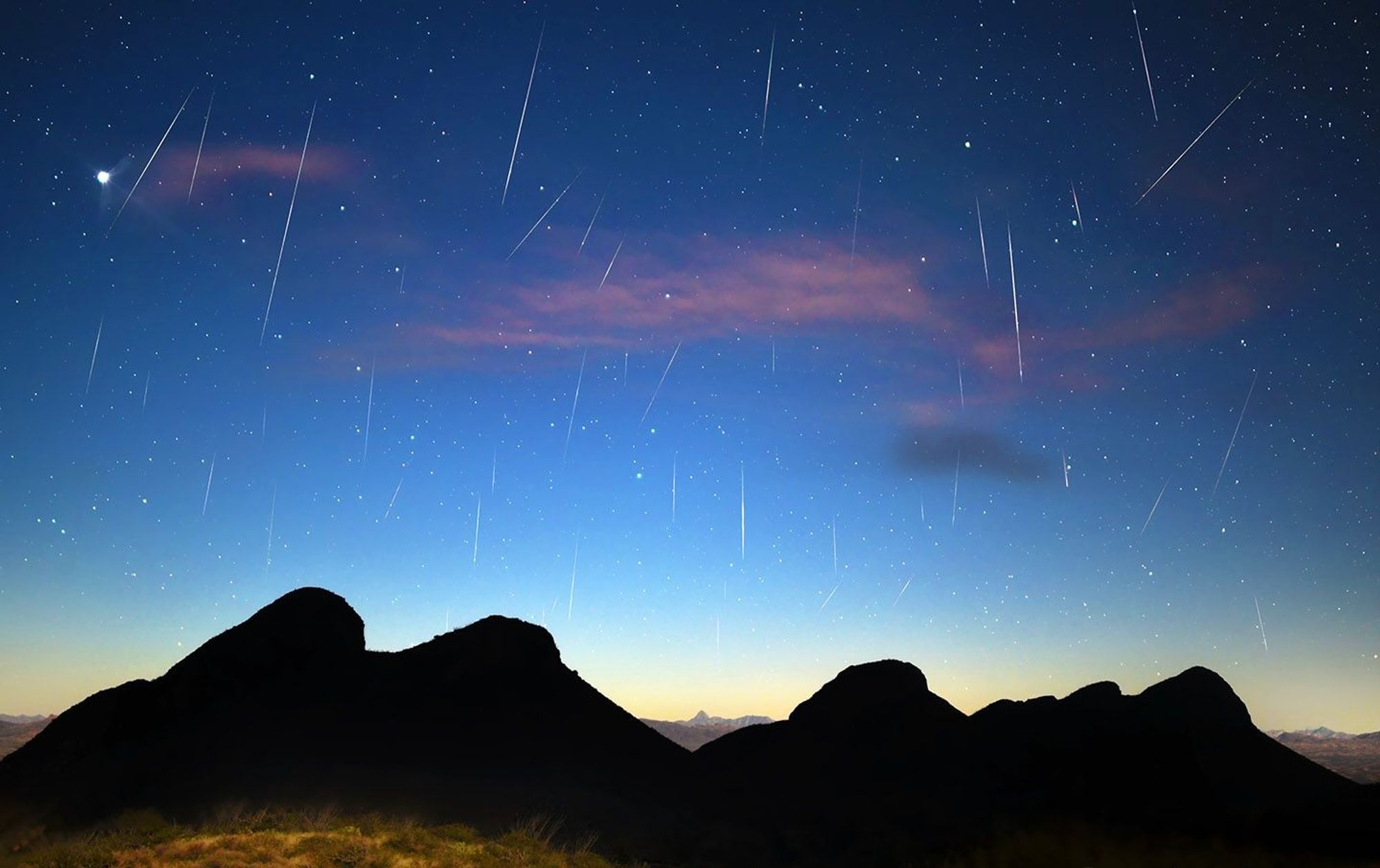A meteor shower over desert land, before night has fallen completely.