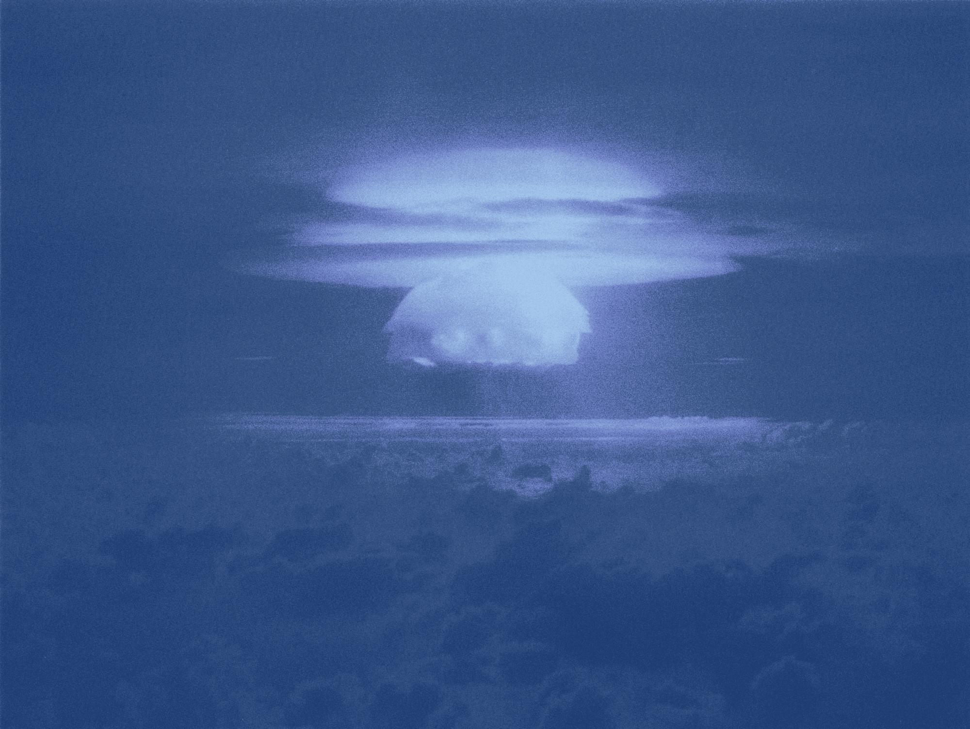 The mushroom-shaped cloud of a nuclear blast photographed from afar.