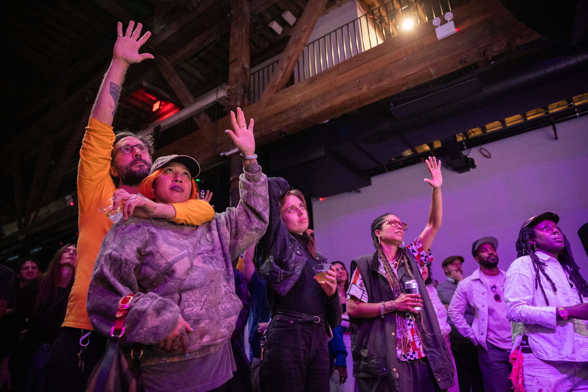 Audience members lit in soft purple raising their hands and looking at an obscured stage