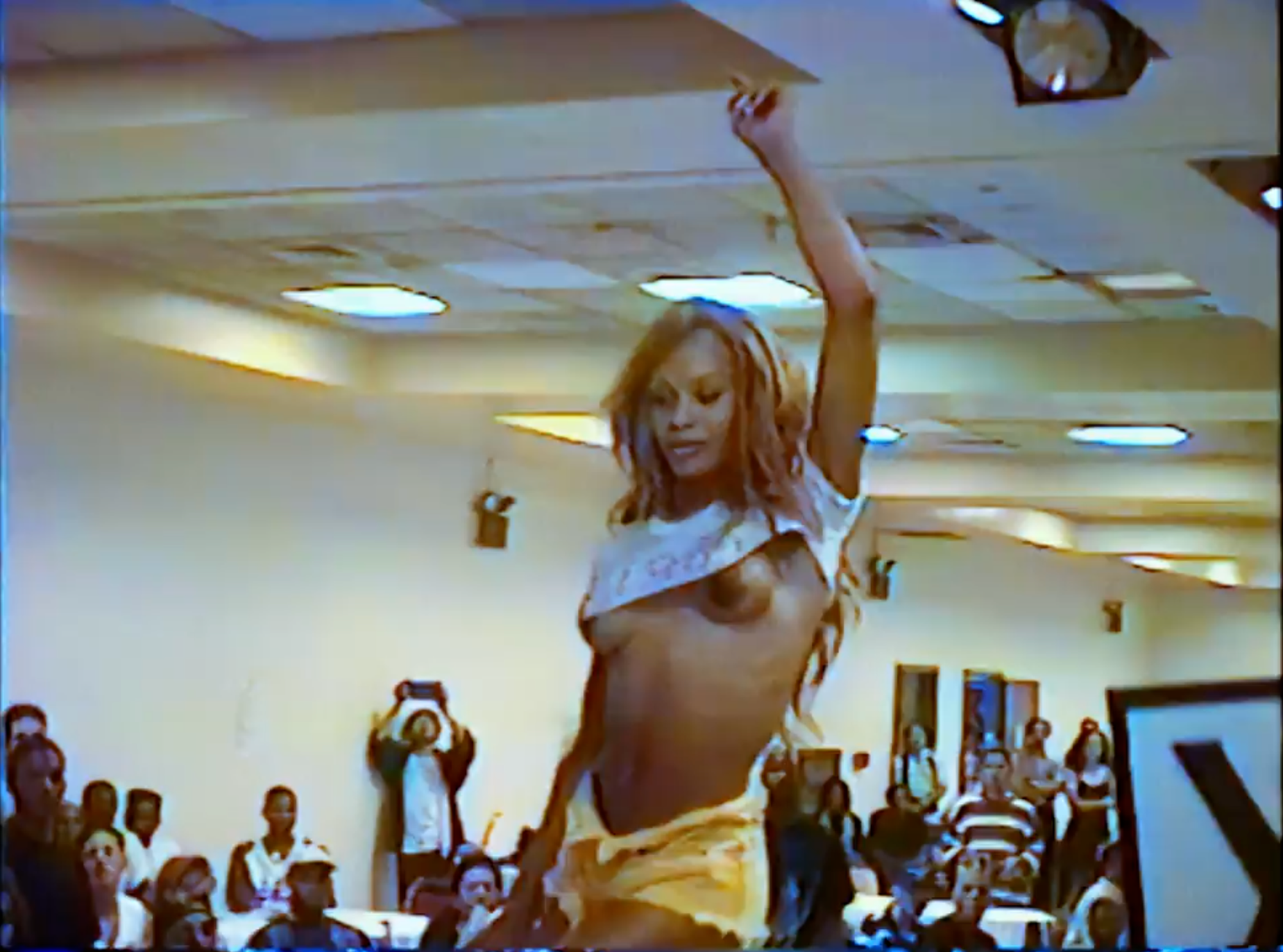 Woman walking through a ball show with hands up and cropped top exposing her breasts