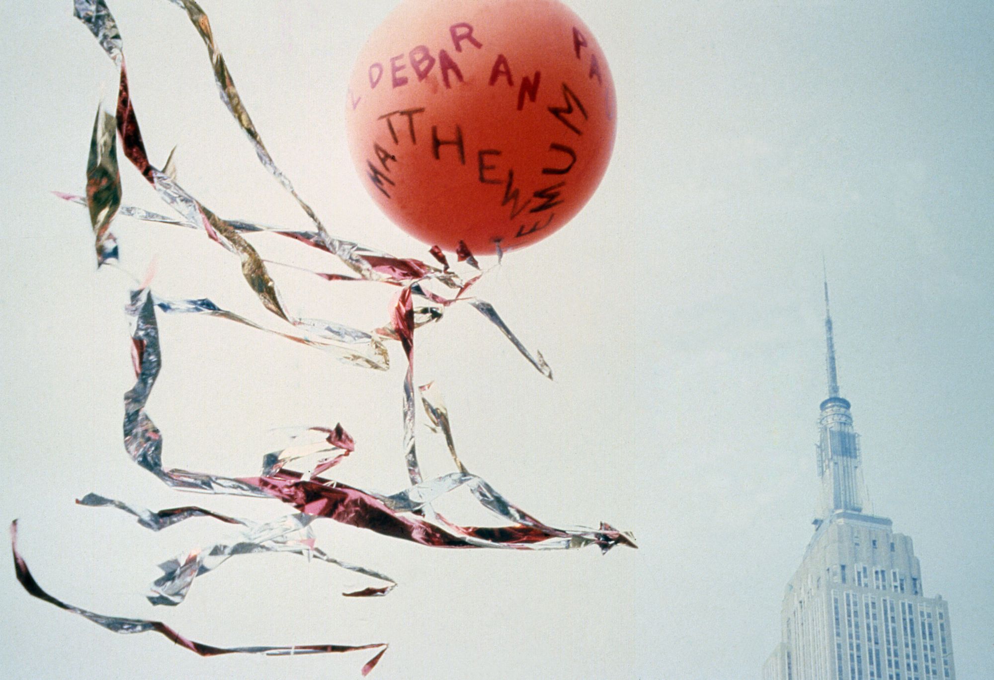 A red balloon with written text tied to tinsel hovers above the Empire State Building.