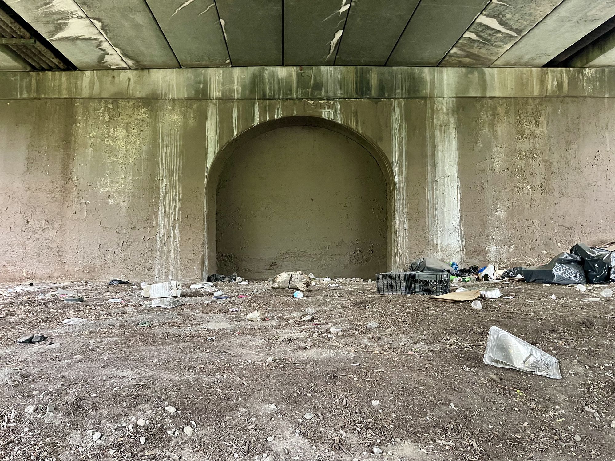 The bleak view from under a bridge, covered in trash.