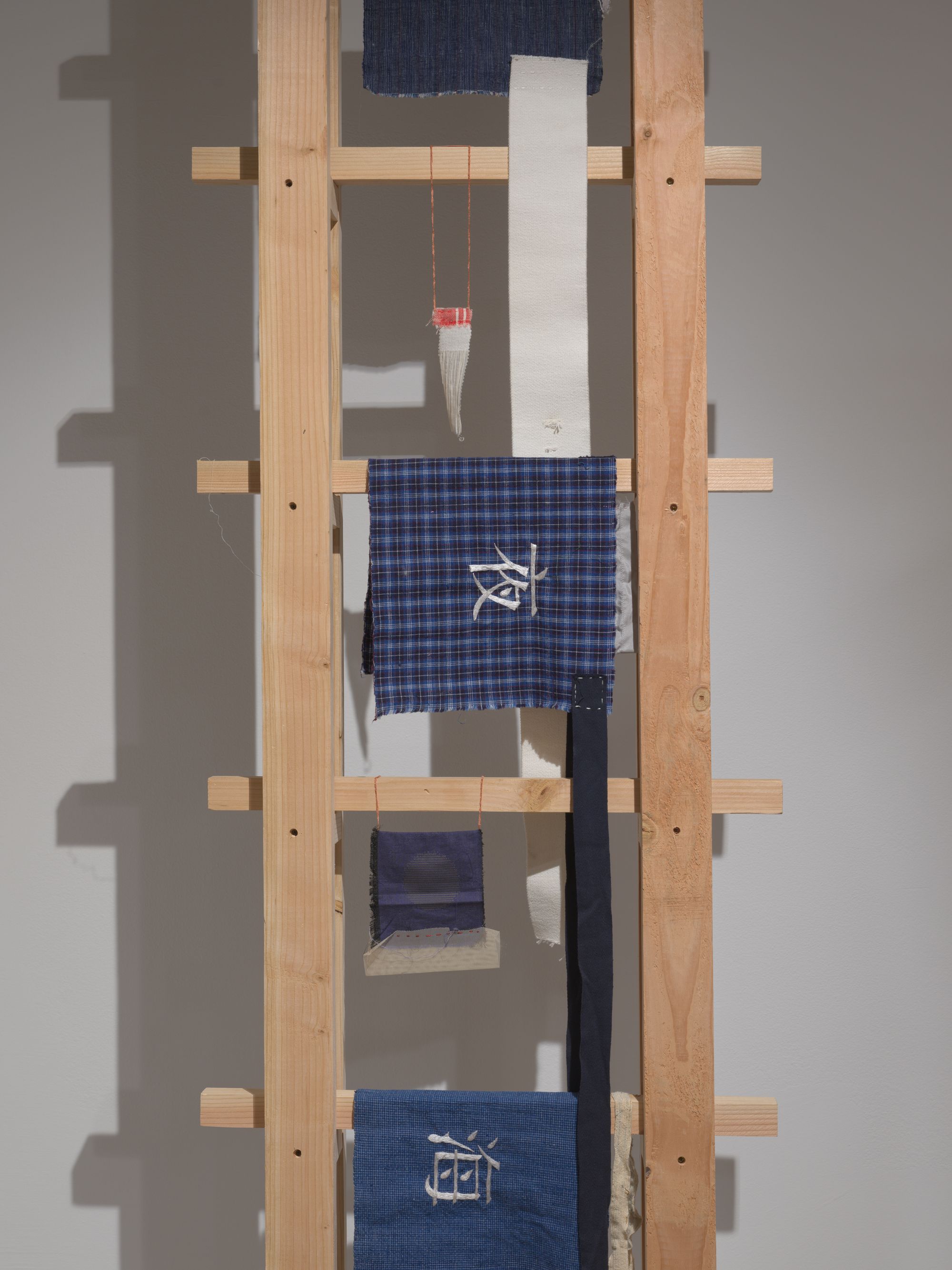 Delicate pieces of dark blue cloth with mandarin characters embroidered hang from a wooden ladder.