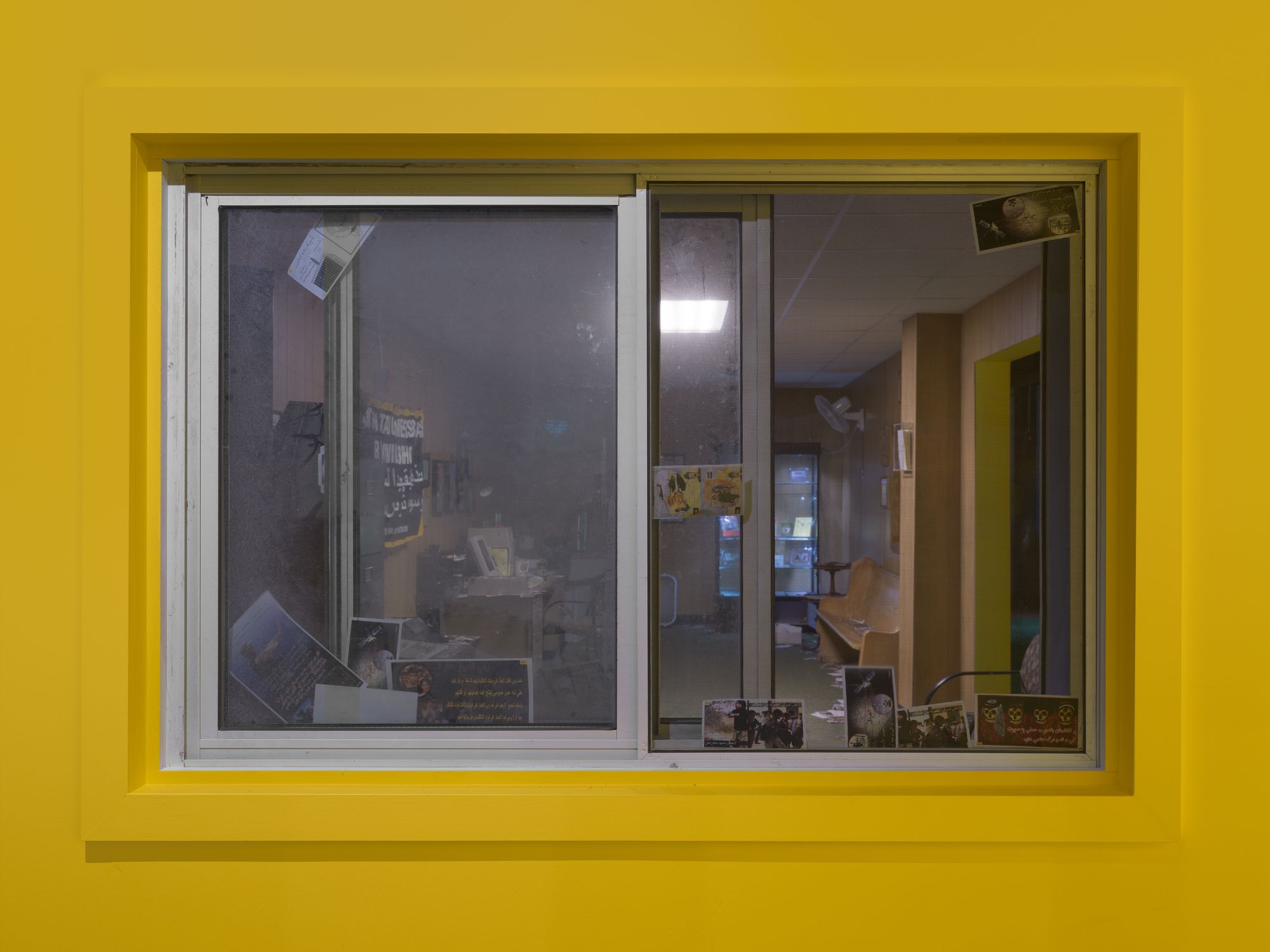 Dirty window on a yellow wall, showing the exhibit inside.