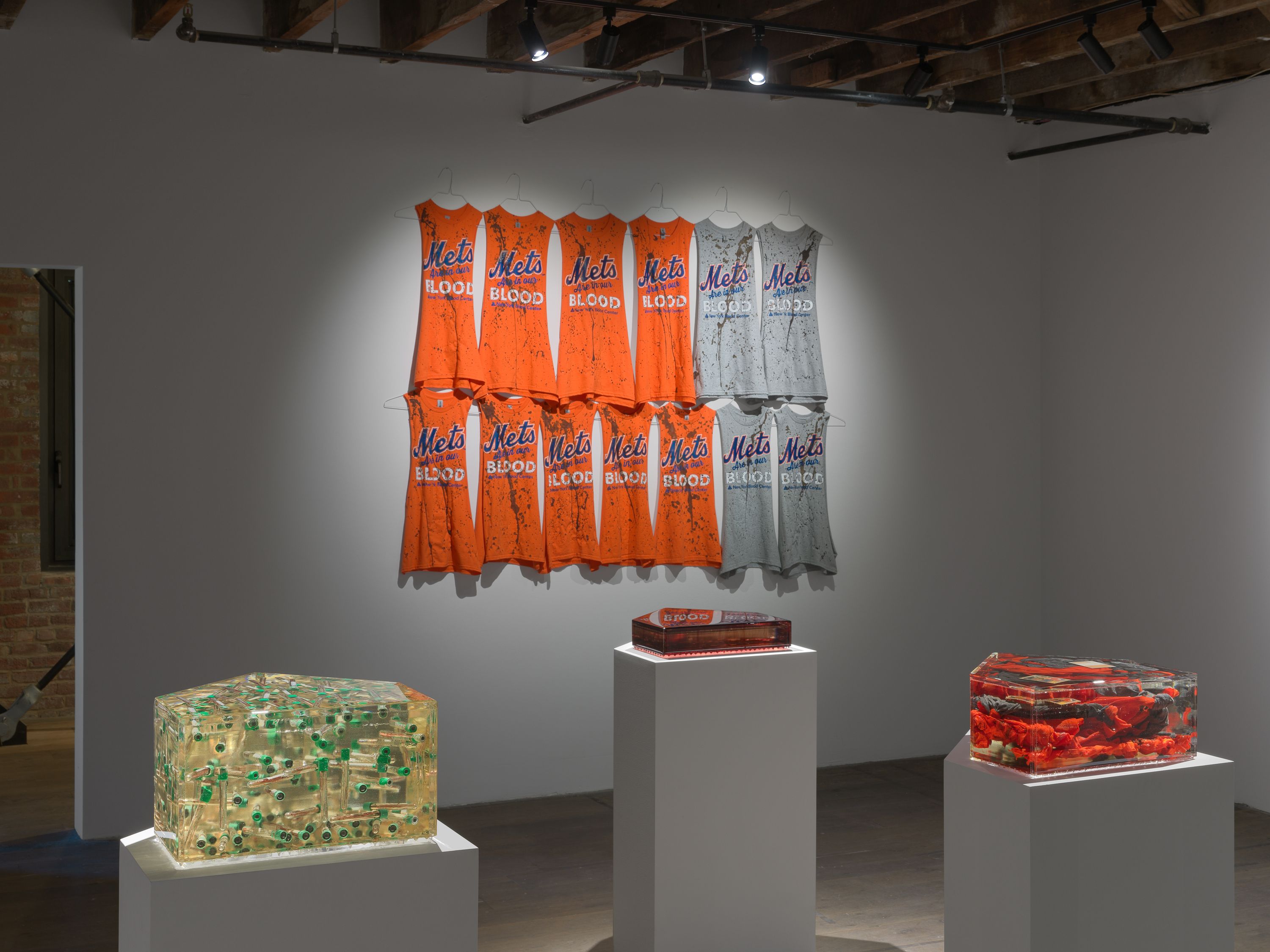 Bases Loaded, a series of baseball t-shirts hung on a white wall in two rows with blood splatterings. 