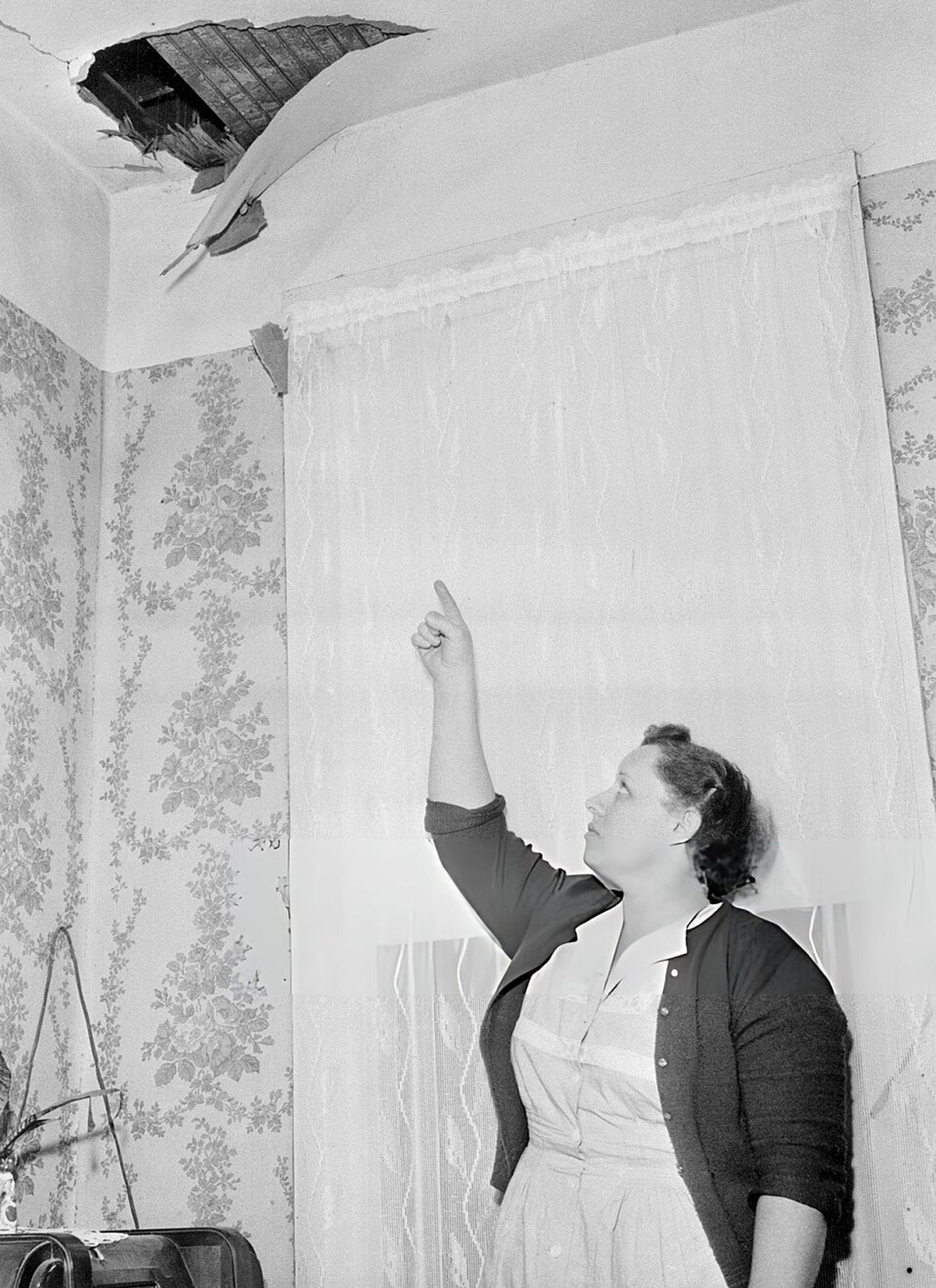 Black and white photograph of white women pointing to the ceiling, which has a hole.