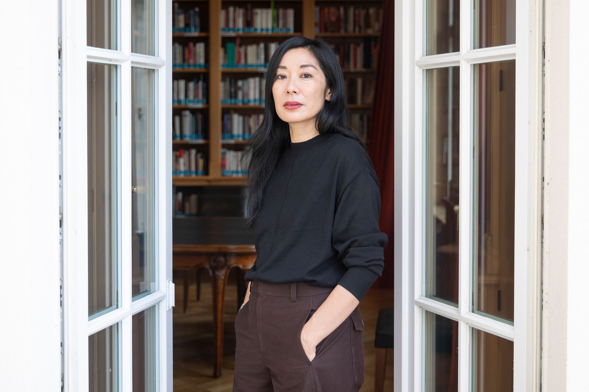 A photograph of Katie Kitamura, looking towards the camera with her hands in her pockets.