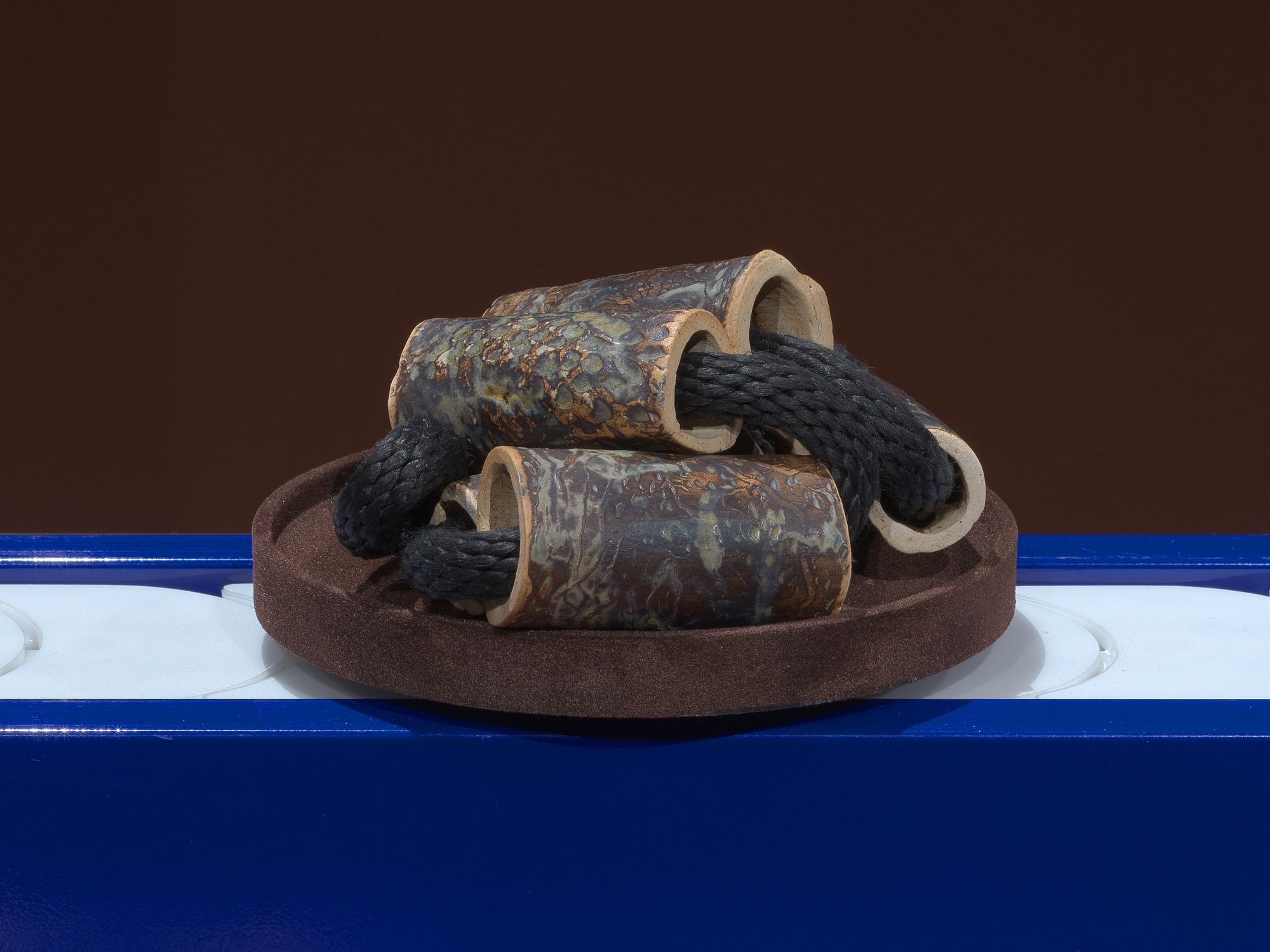 A large black cord, running through objects that resemble hollow bones, is placed on a brown plate that moves along a blue conveyor belt.