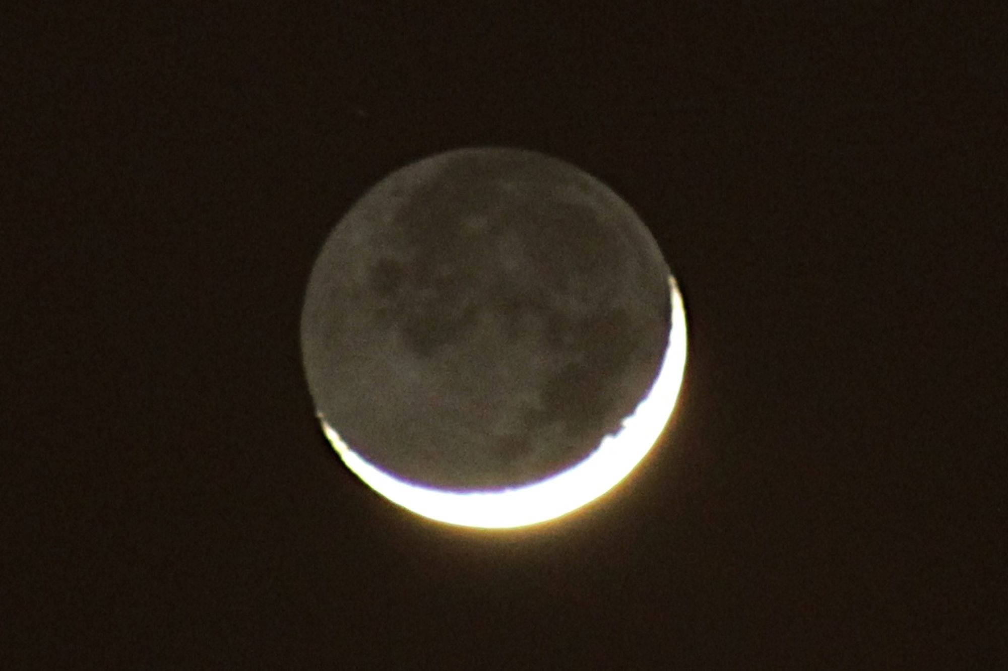 A sliver of bright moon lines the otherwise darkened planet.