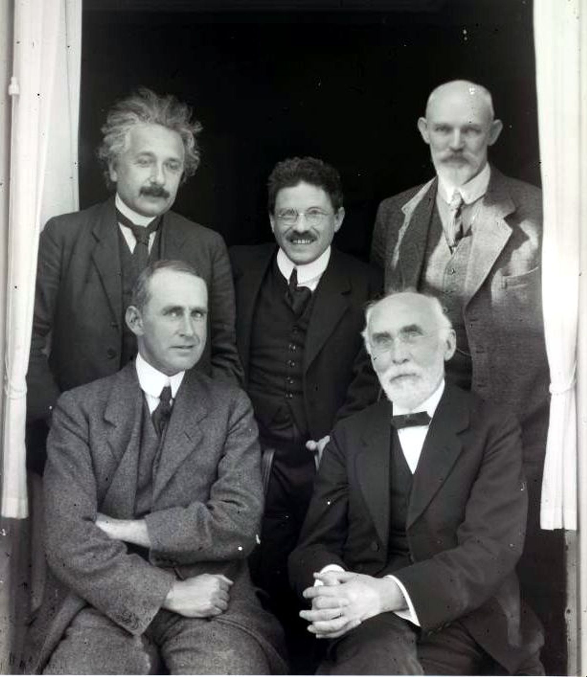 A black-and-white photograph of five famous physicists posing for the camera, all smiling.