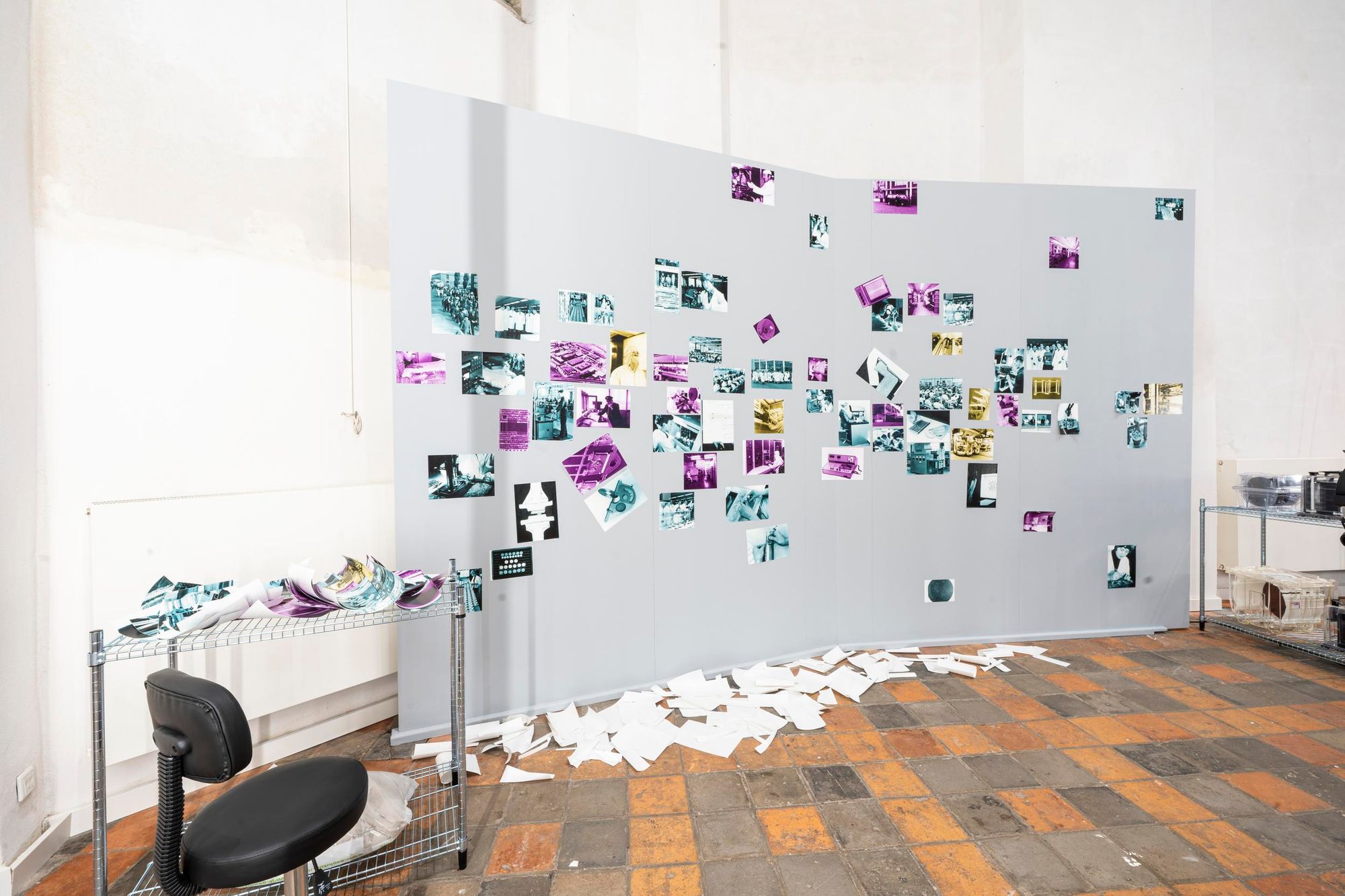 A free-floating gray backdrop stands against a white wall, covered in photos of different colors and sizes.