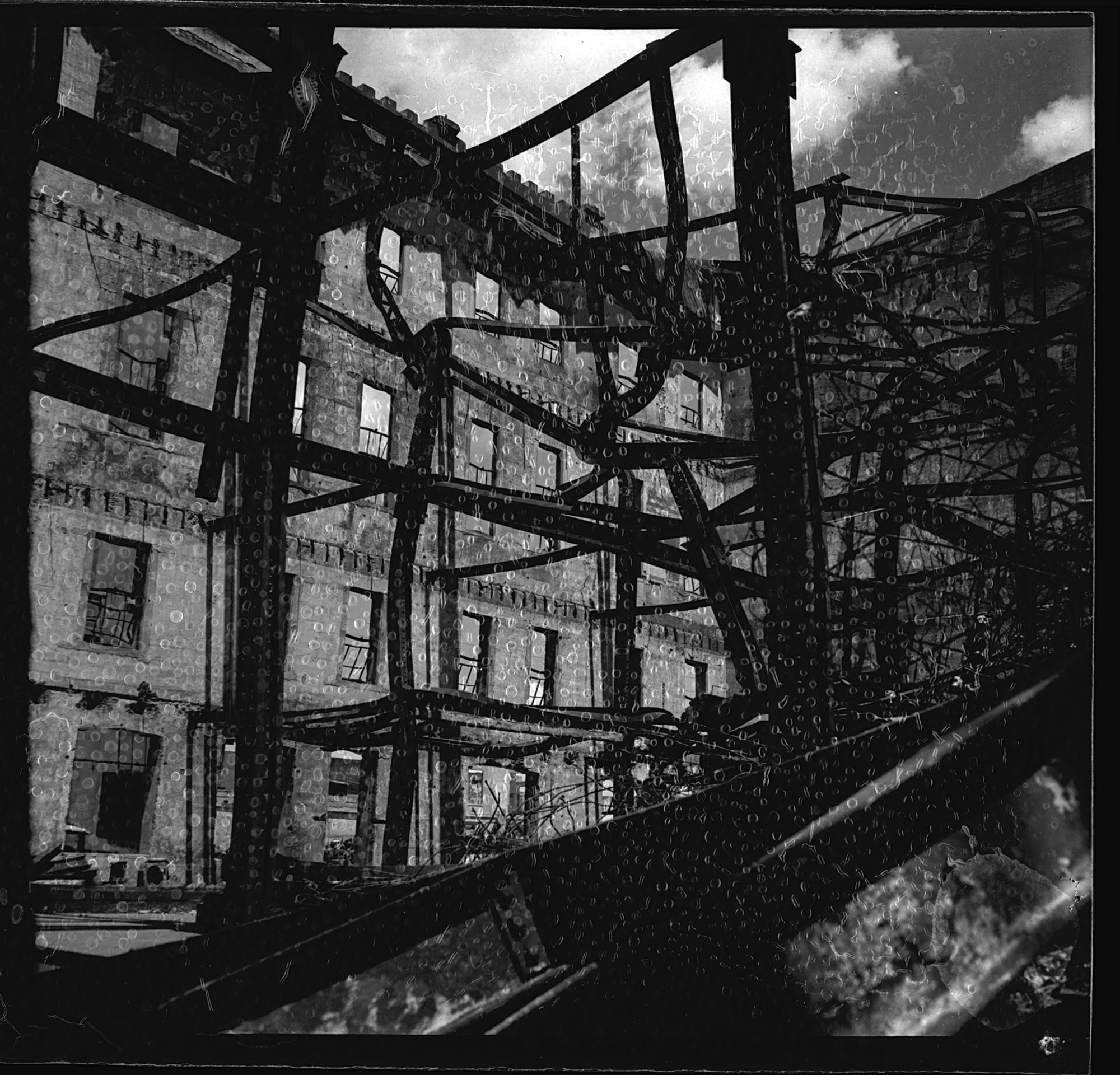 A black-and-white photograph that shows the beams of the American Hardware building in the foreground and another building in the background. There are white circular squiggles on the print.