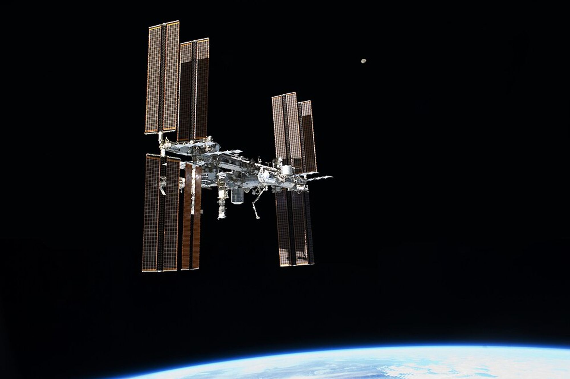 International Space Station flying over the Earth with the Moon faraway in the background.