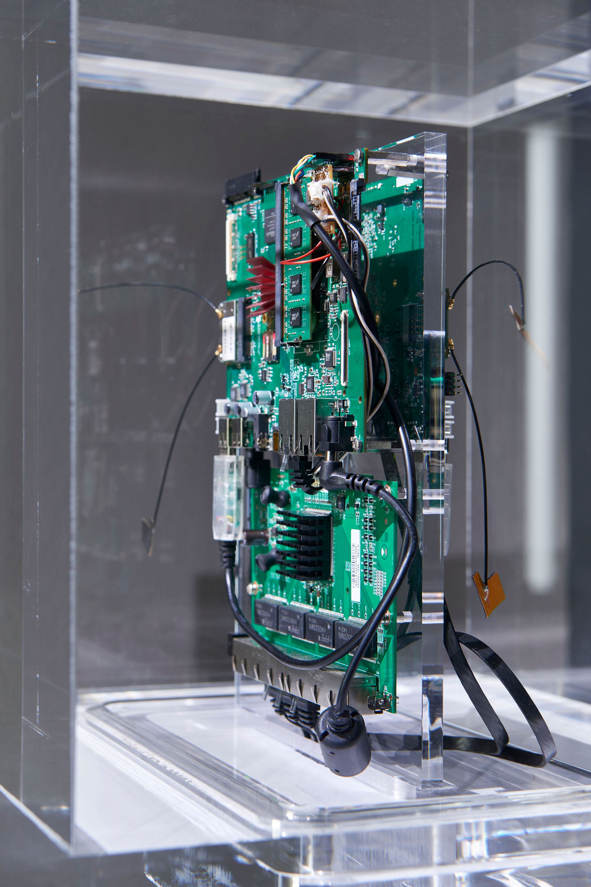 A sculpture that resembles a computer motherboard is displayed in a clear vitrine box.