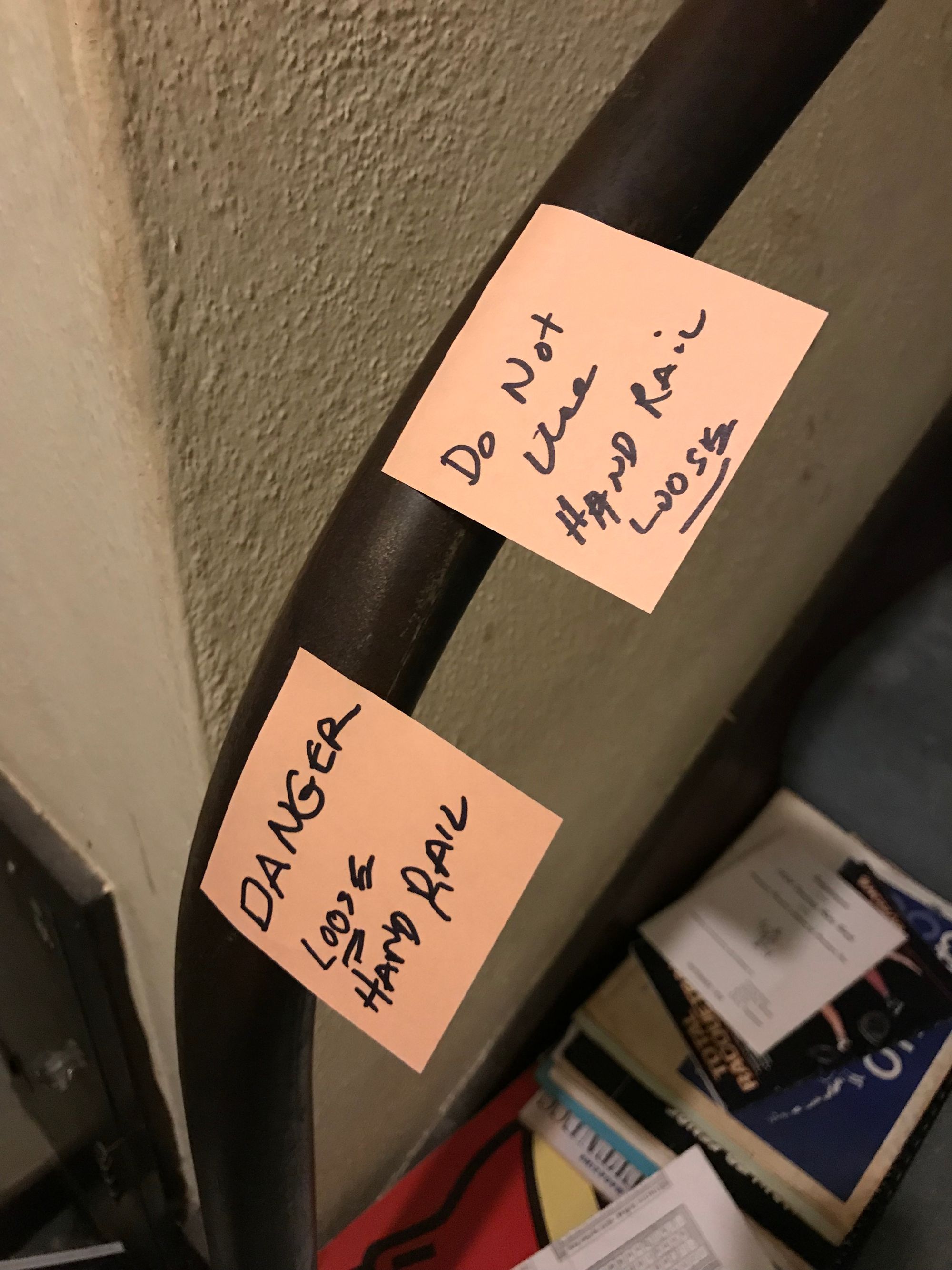 A handrail with sticky notes on it reading "DANGER: Loose Hand Rail" and "Do not use, hand rail loose."