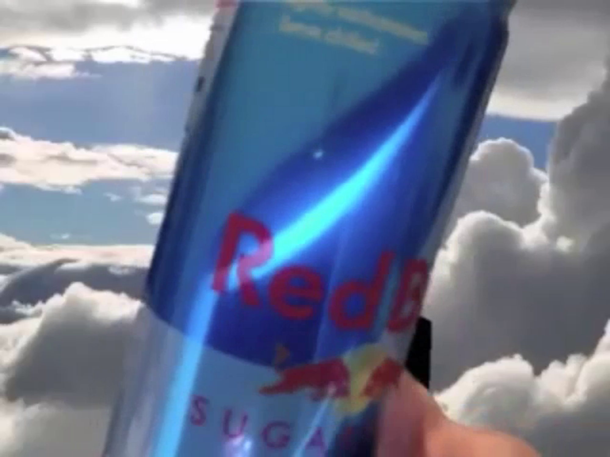 A Red Bull can pushed toward the front of the camera, with a background of a blue sky and clouds