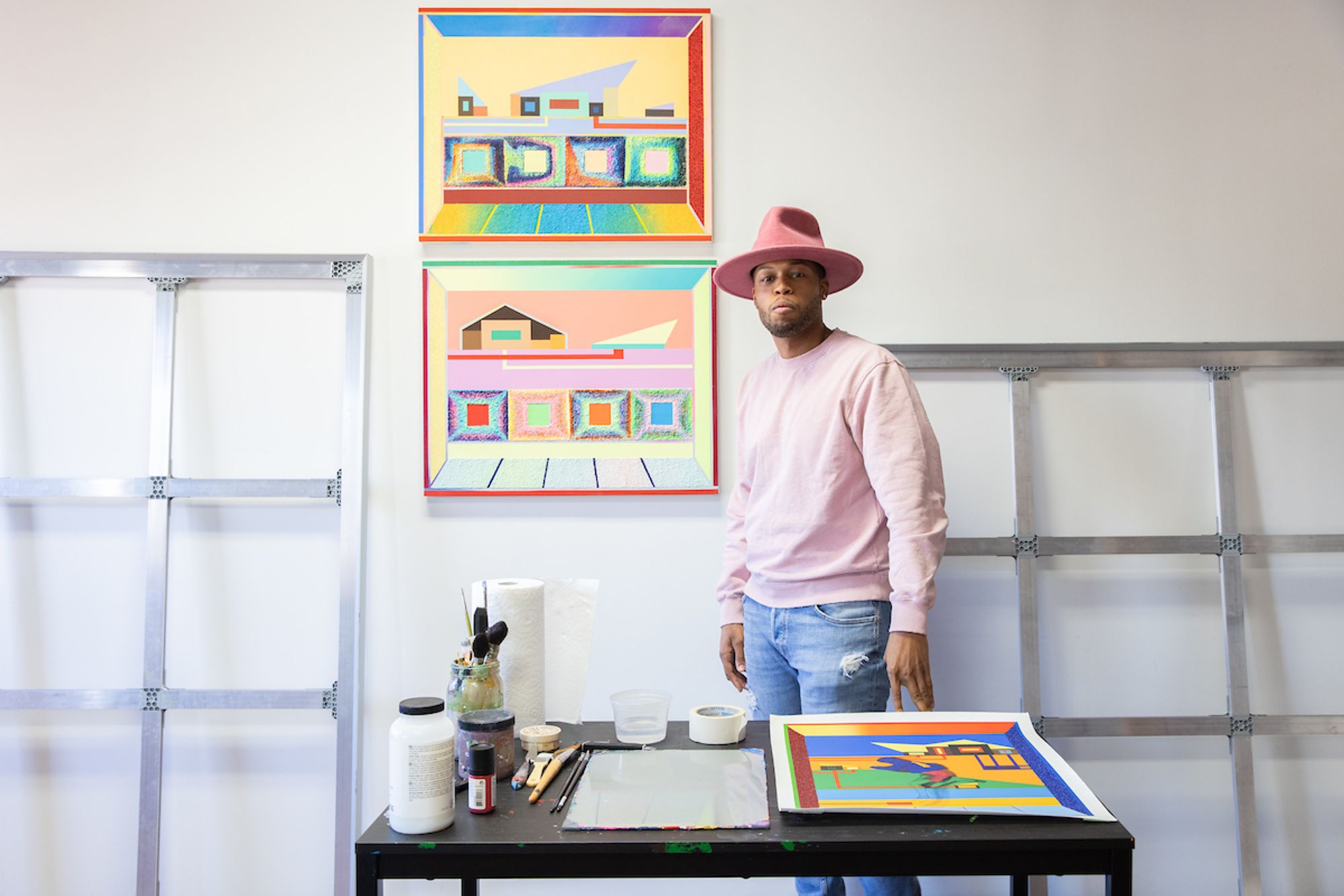 Artist in pink hat in front of colorful canvas