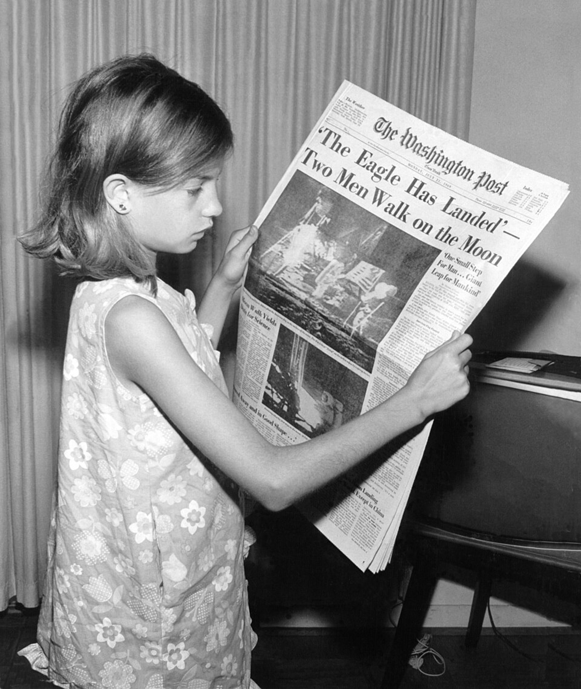 Black and white picture of a young girl holding a newspaper. Headline reads "The Eagle has Landed -- Two Men Walk on the Moon."