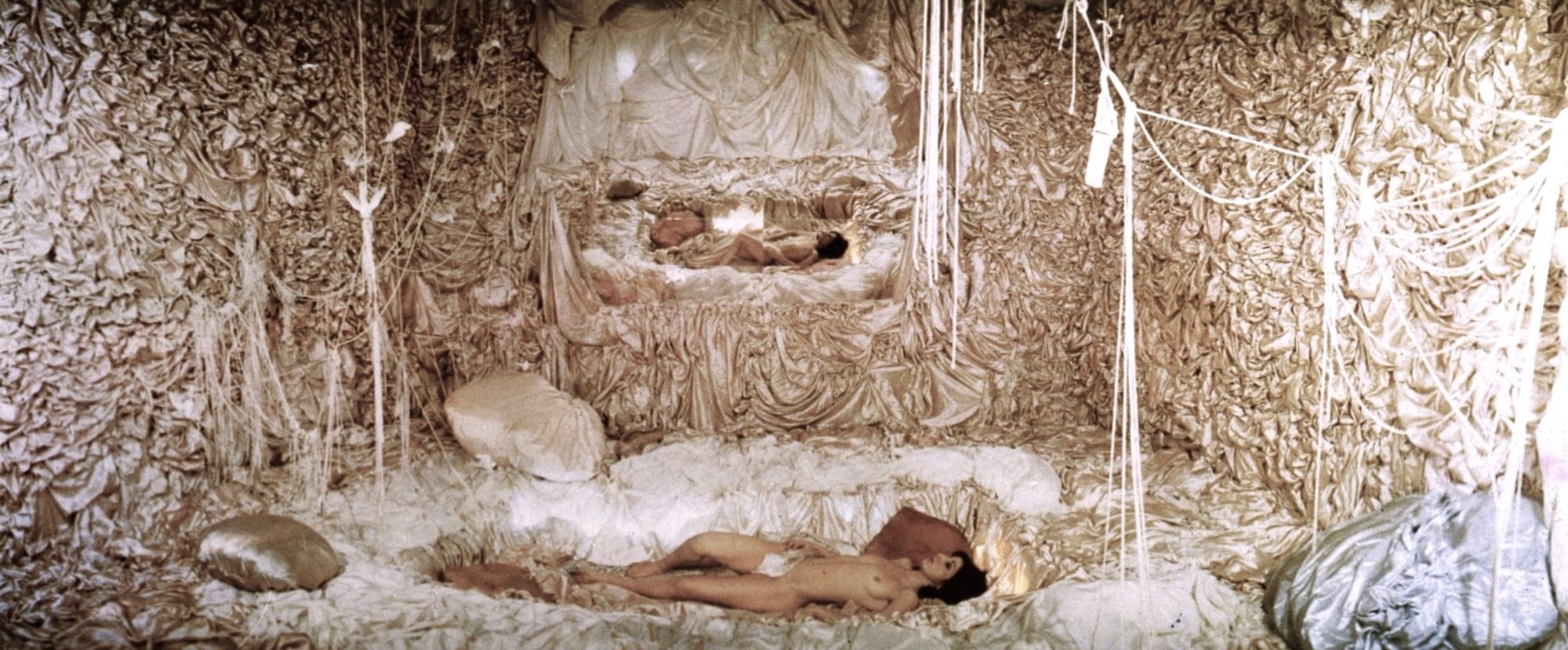 A naked woman slumbers in a room festooned with beige silk and string.