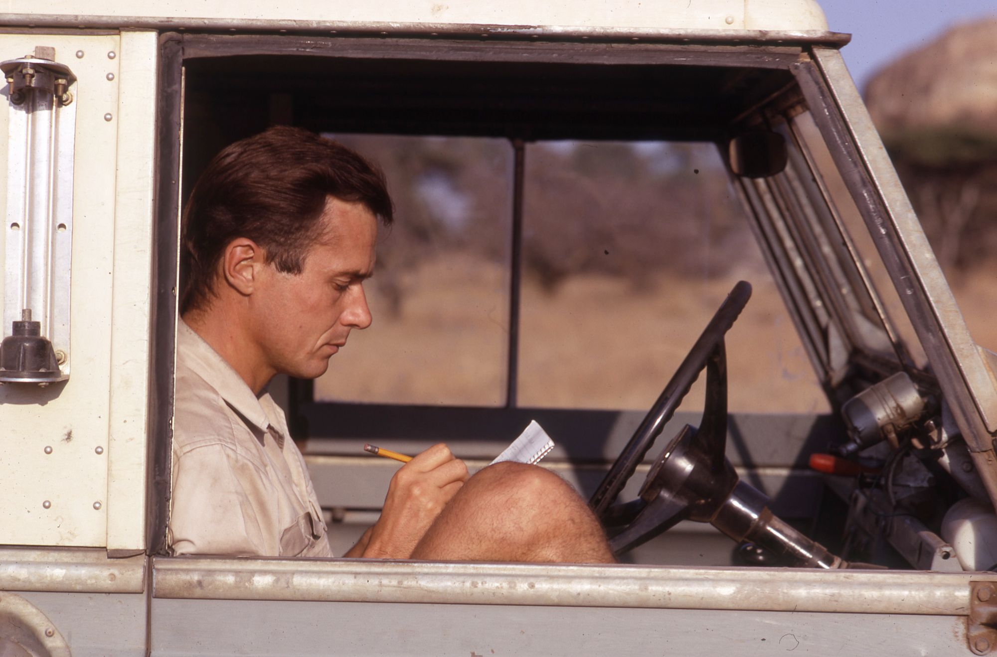 George Schaller sitting in the front seat of a car, writing notes on paper.