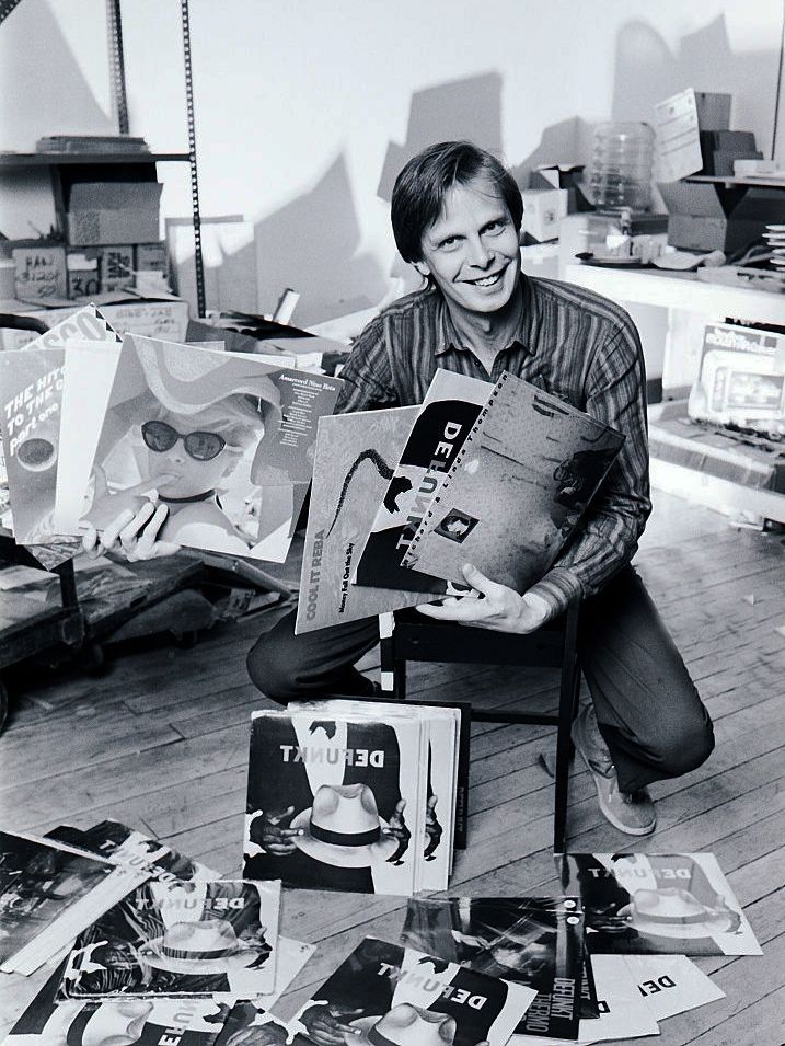 A man smiles at the camera, holding stacks of Defunkt records.