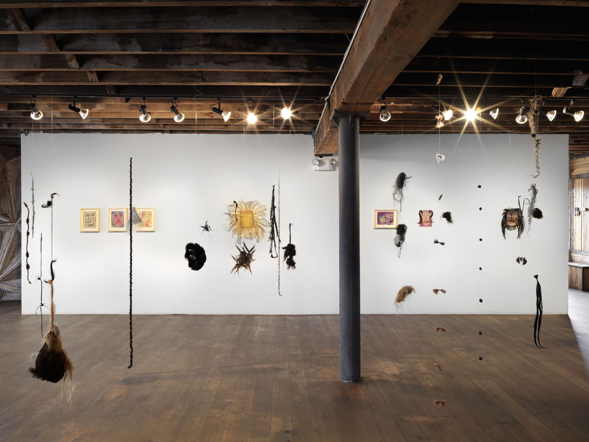 An installation view of "Spirits of Manhattan," featuring hanging wigs in Pioneer Works' industrial space