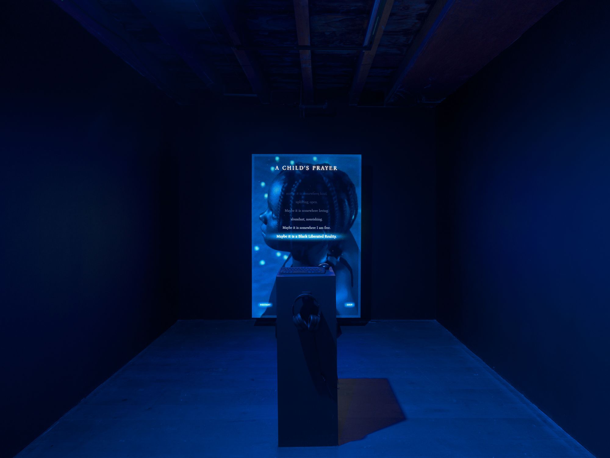 A screen in a dark room that reads "A CHILD'S PRAYER" with an image of a young black girl behind it.