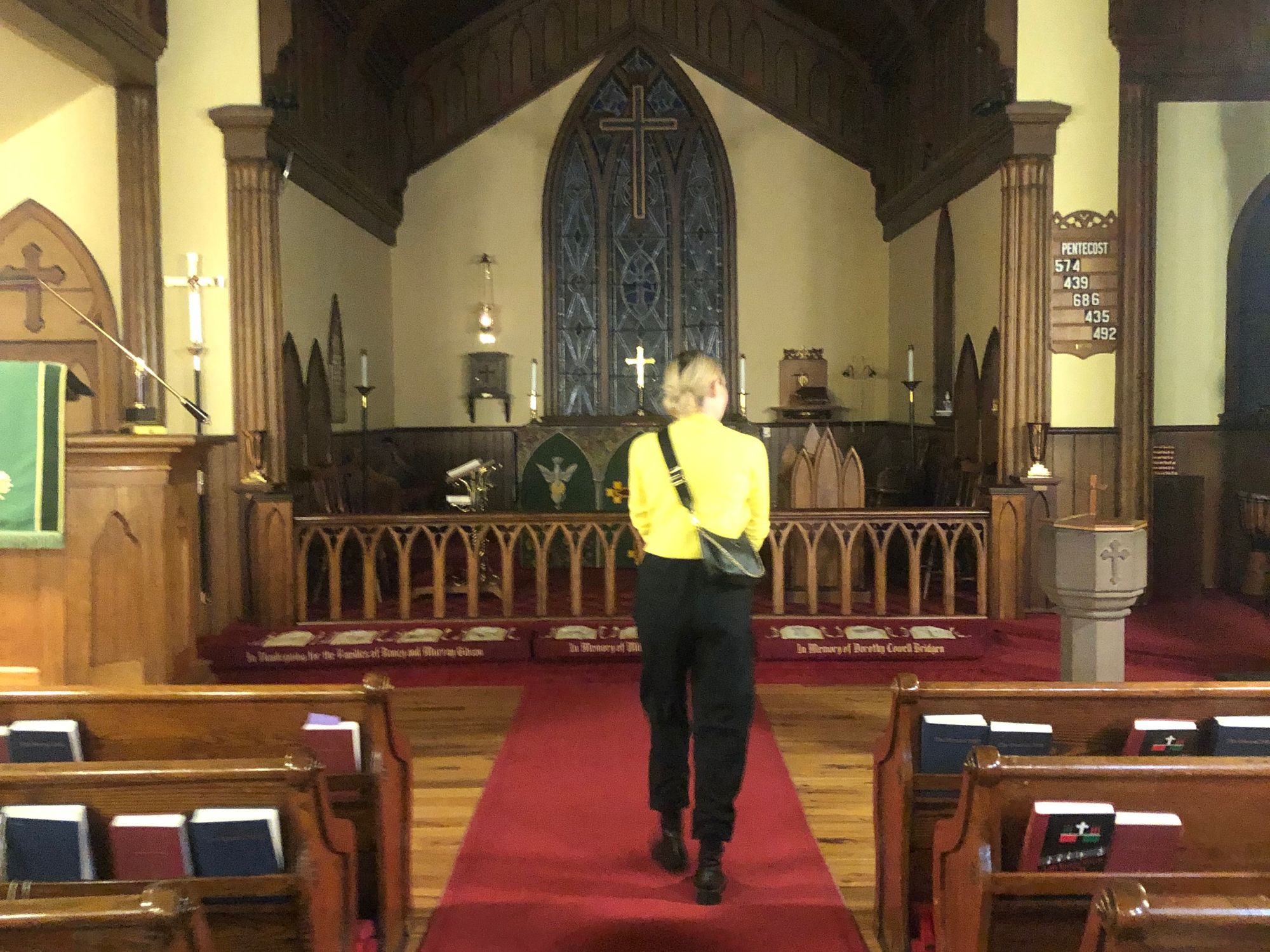 A blond woman walks down the aisle of a church, towards the organ at its center.