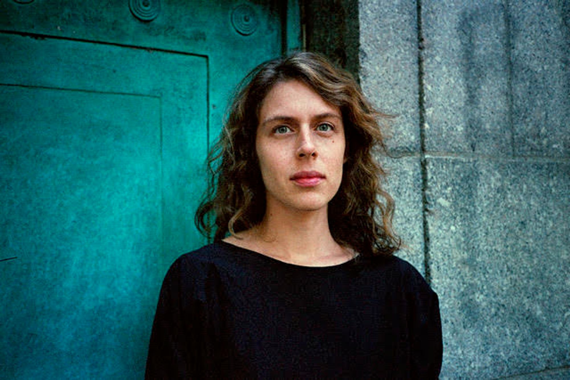 Rachel Aviv, photographed in front of a blue-green doorway.