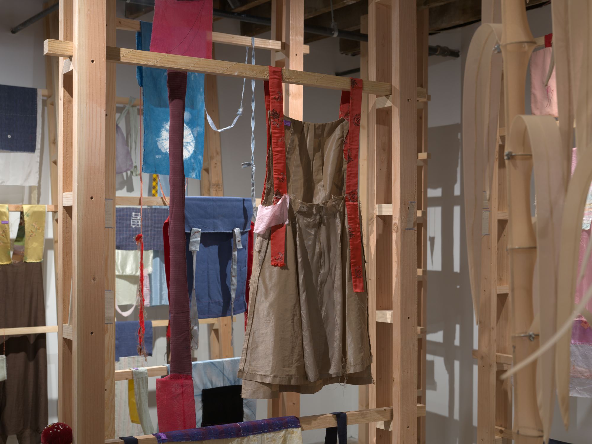 Hand-sewn garments hanging from wooden planks in a gallery space.