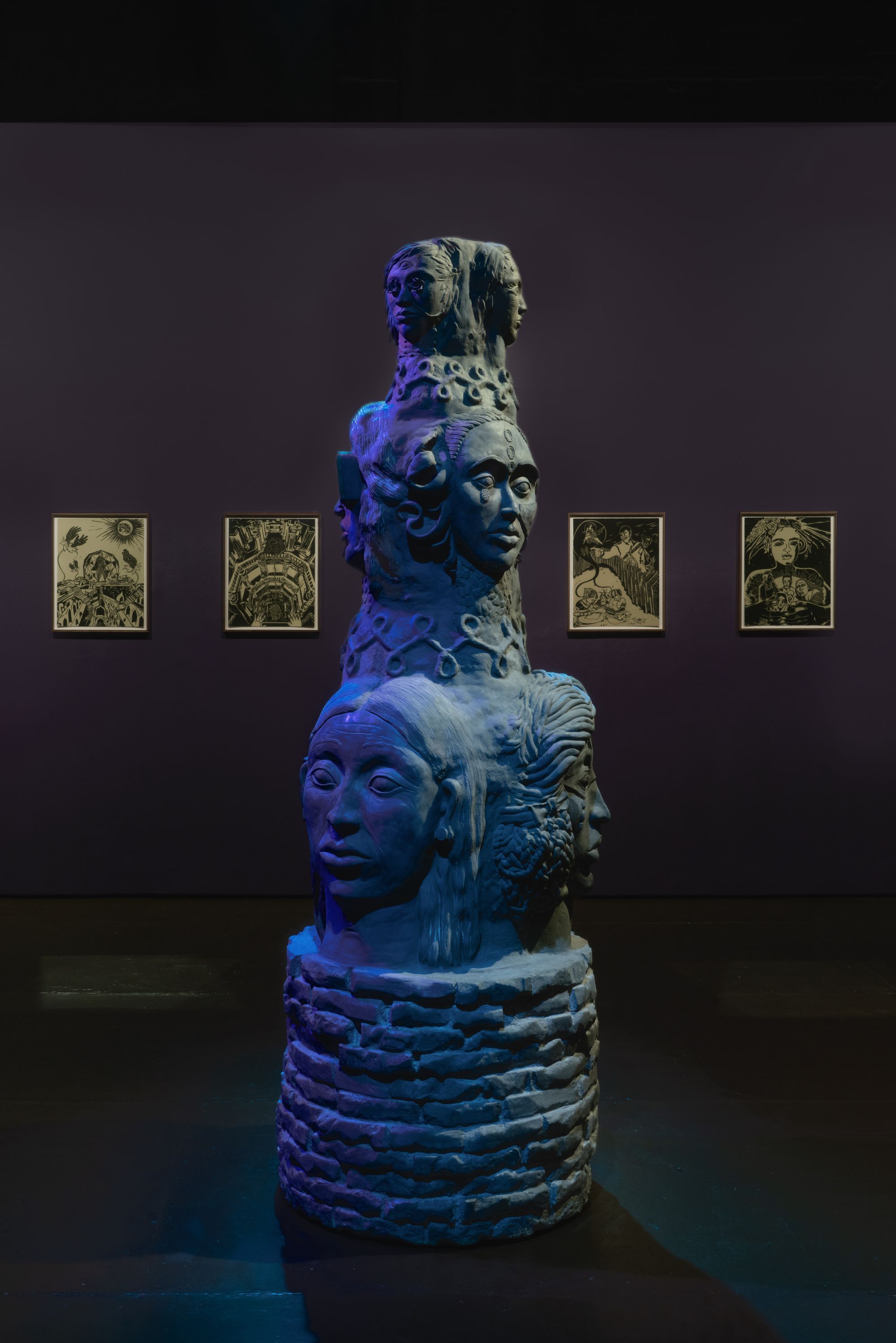 A tall column of faces is tinged blue, while a wall in back onto which prints are hung is also tinged blue.