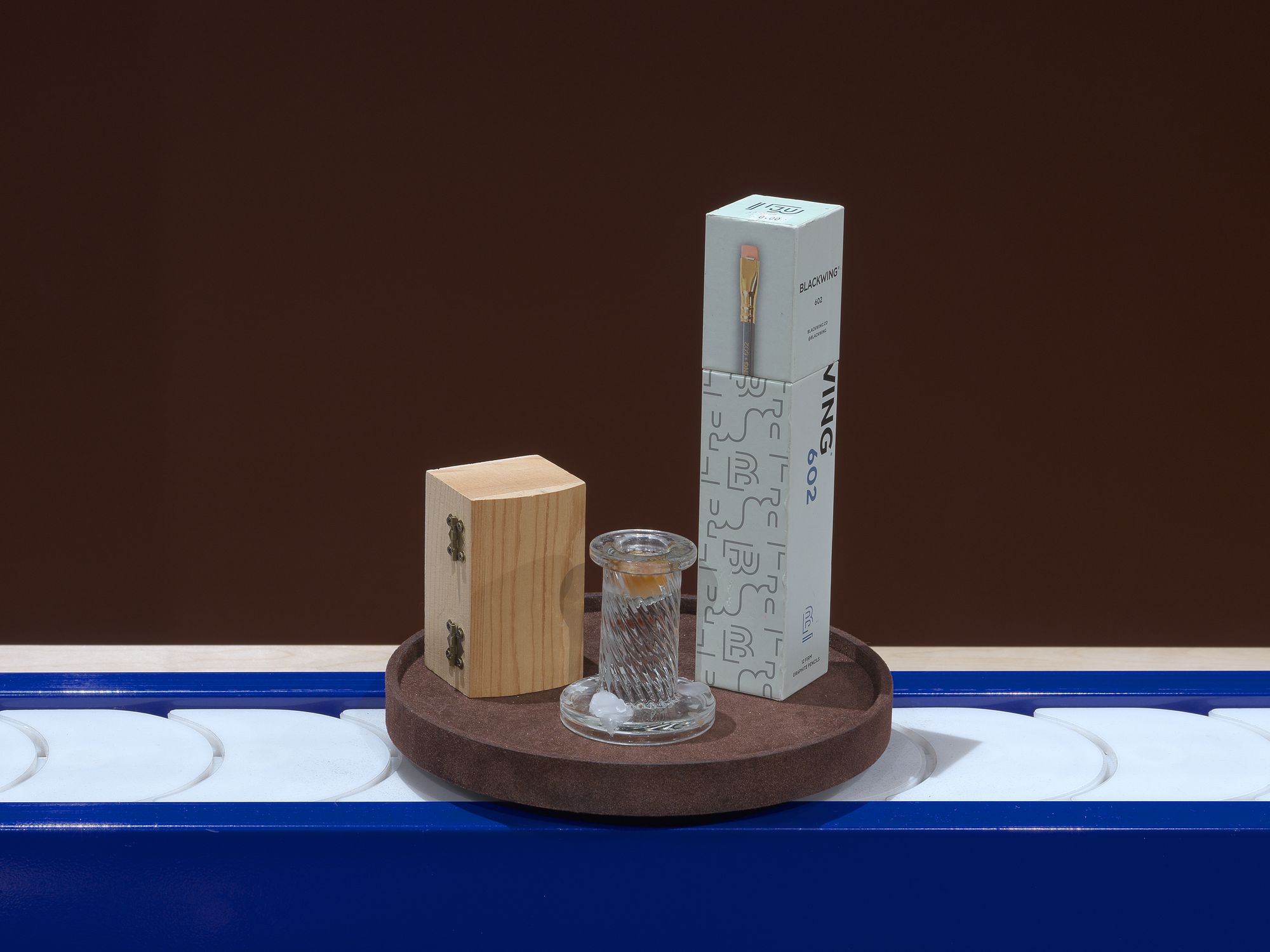 A pencil, a candlestick, and a wooden box on a conveyor belt.