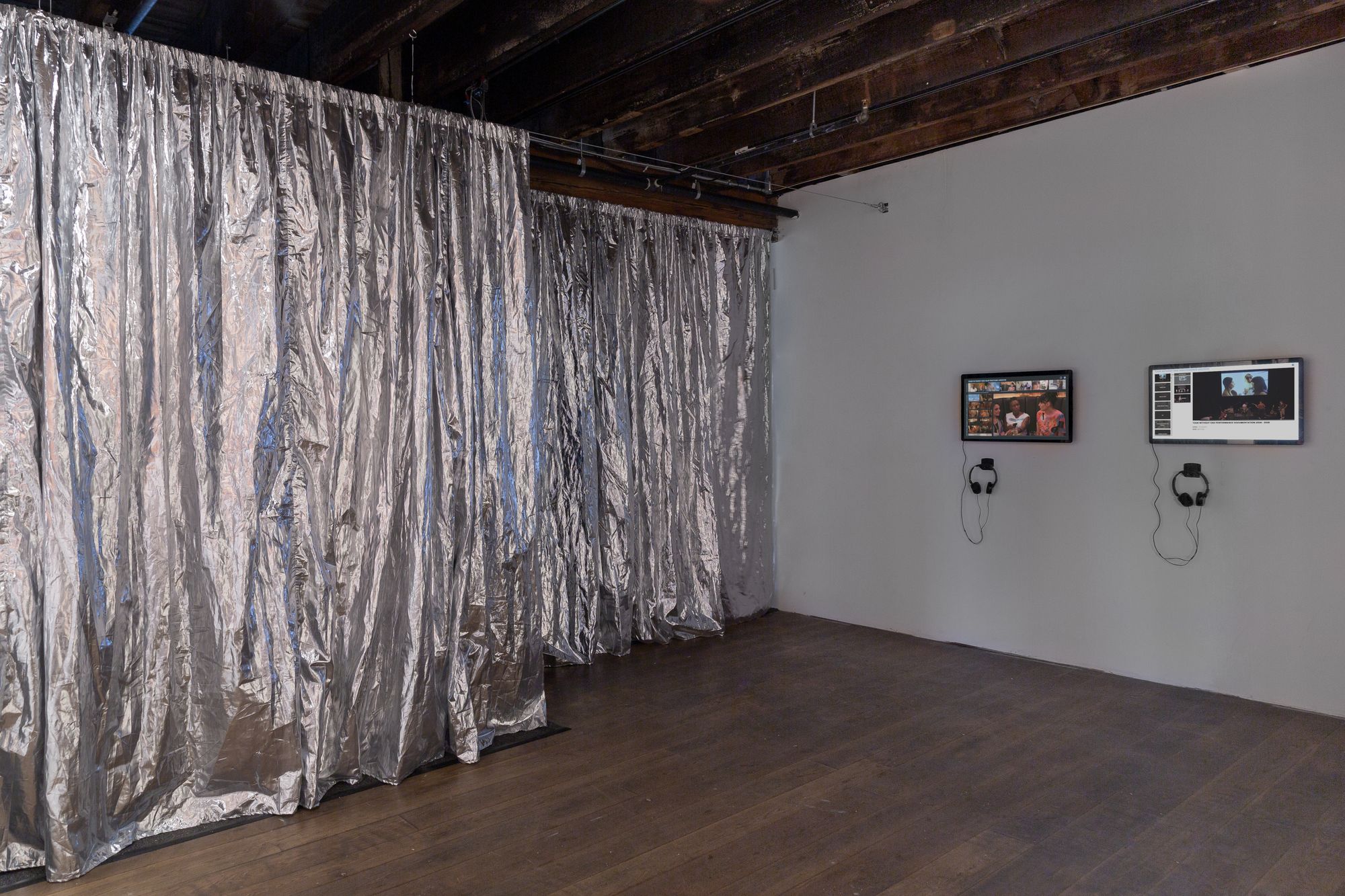 An angled view of silvery lame curtains and two flat screen, touchstone monitors of archival footage of performances in various spaces and outtakes from the film Tour Without End.