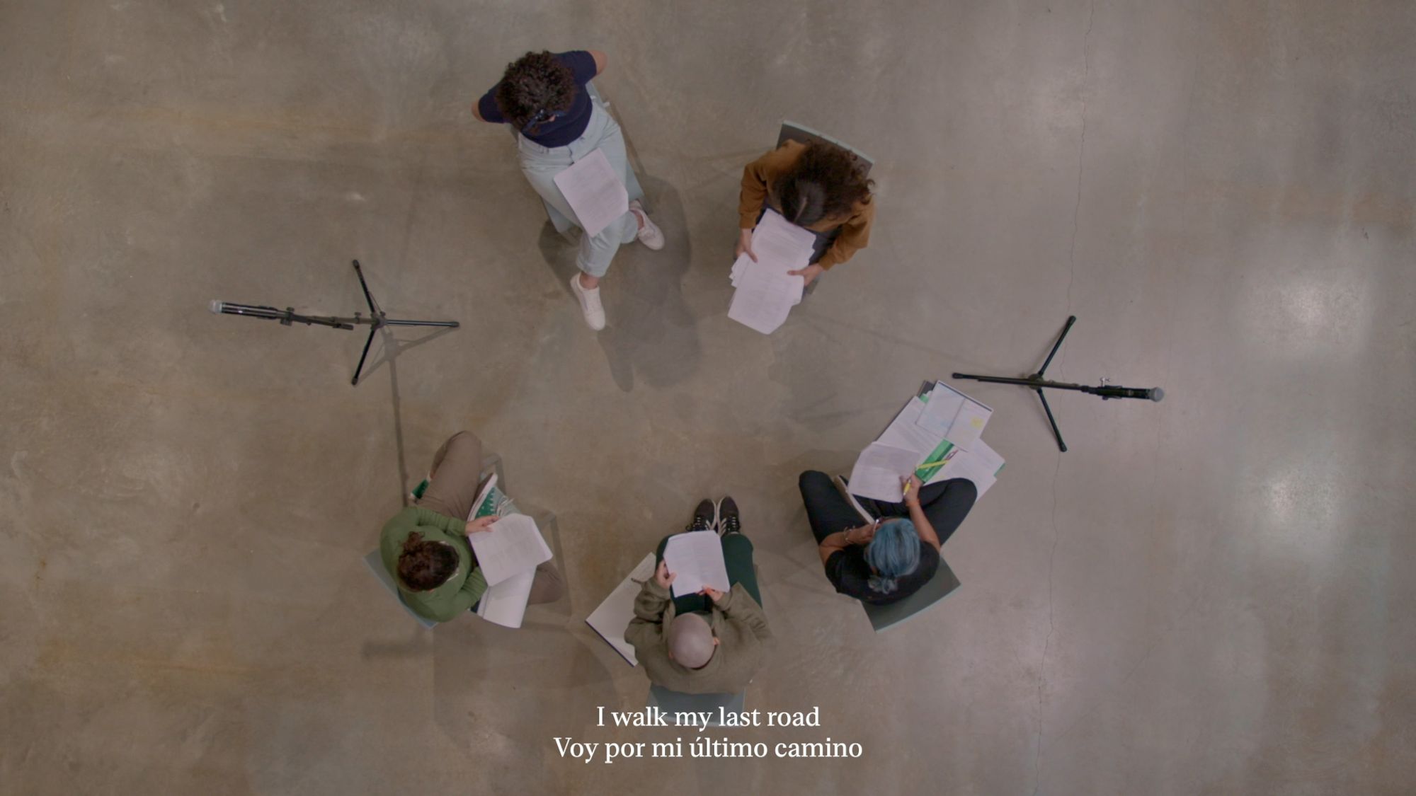 A birds-eye view of people sitting in a circle, reading from paper held on each lap. 