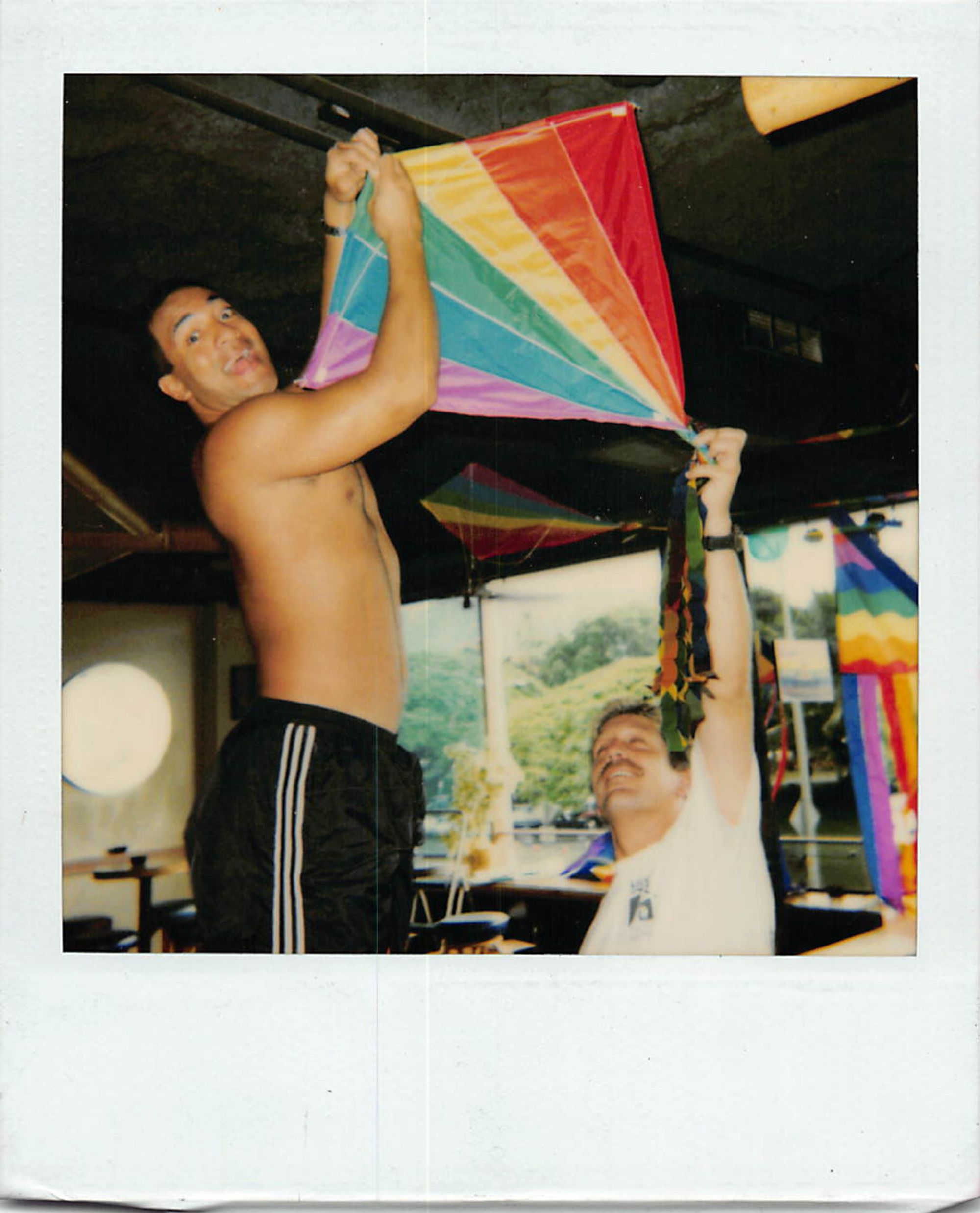  A polaroid of two men hanging up a pride-themed kite.