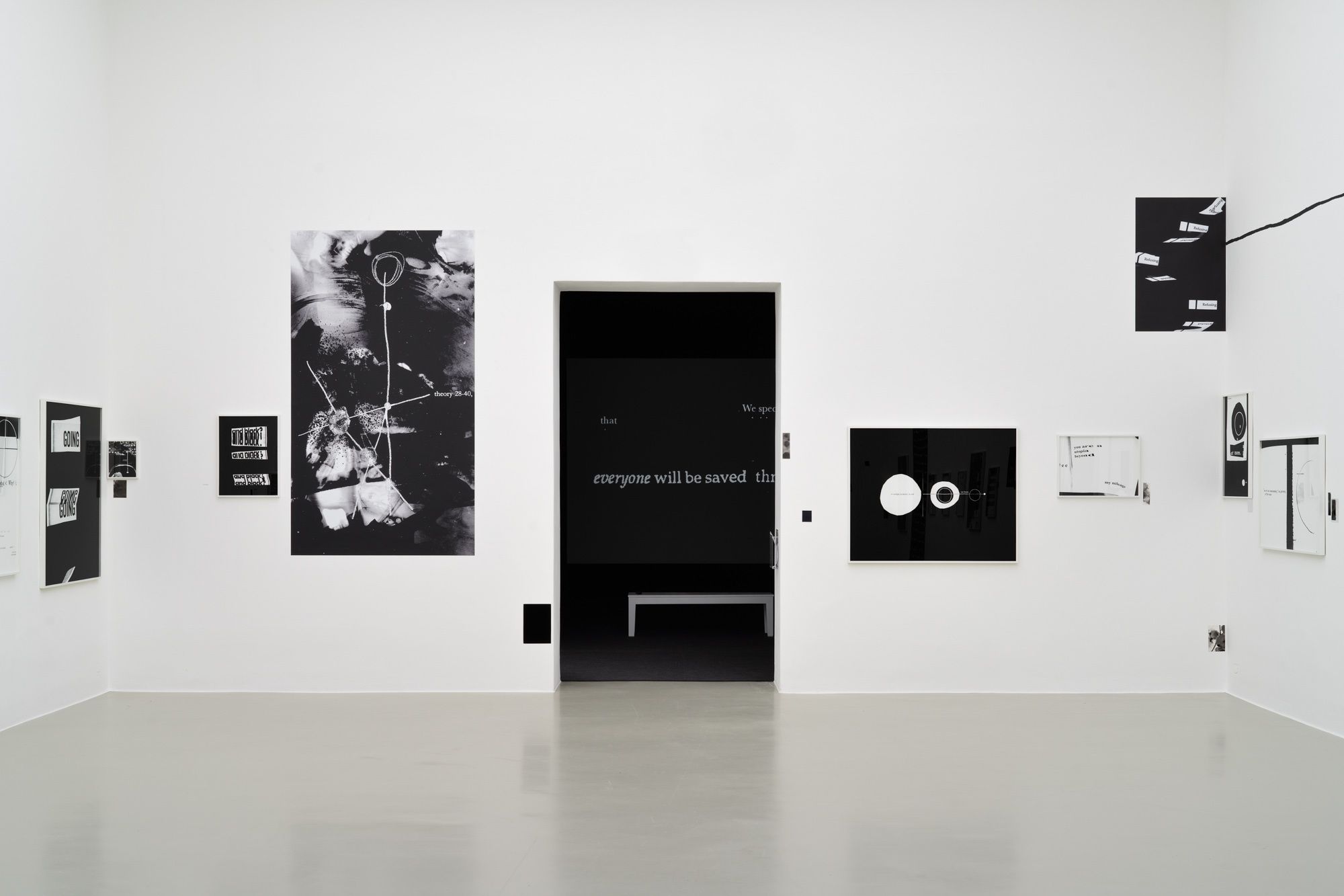 An image of a white-walled gallery space covered in black artworks, with a dark rectangular doorway centered on the wall.