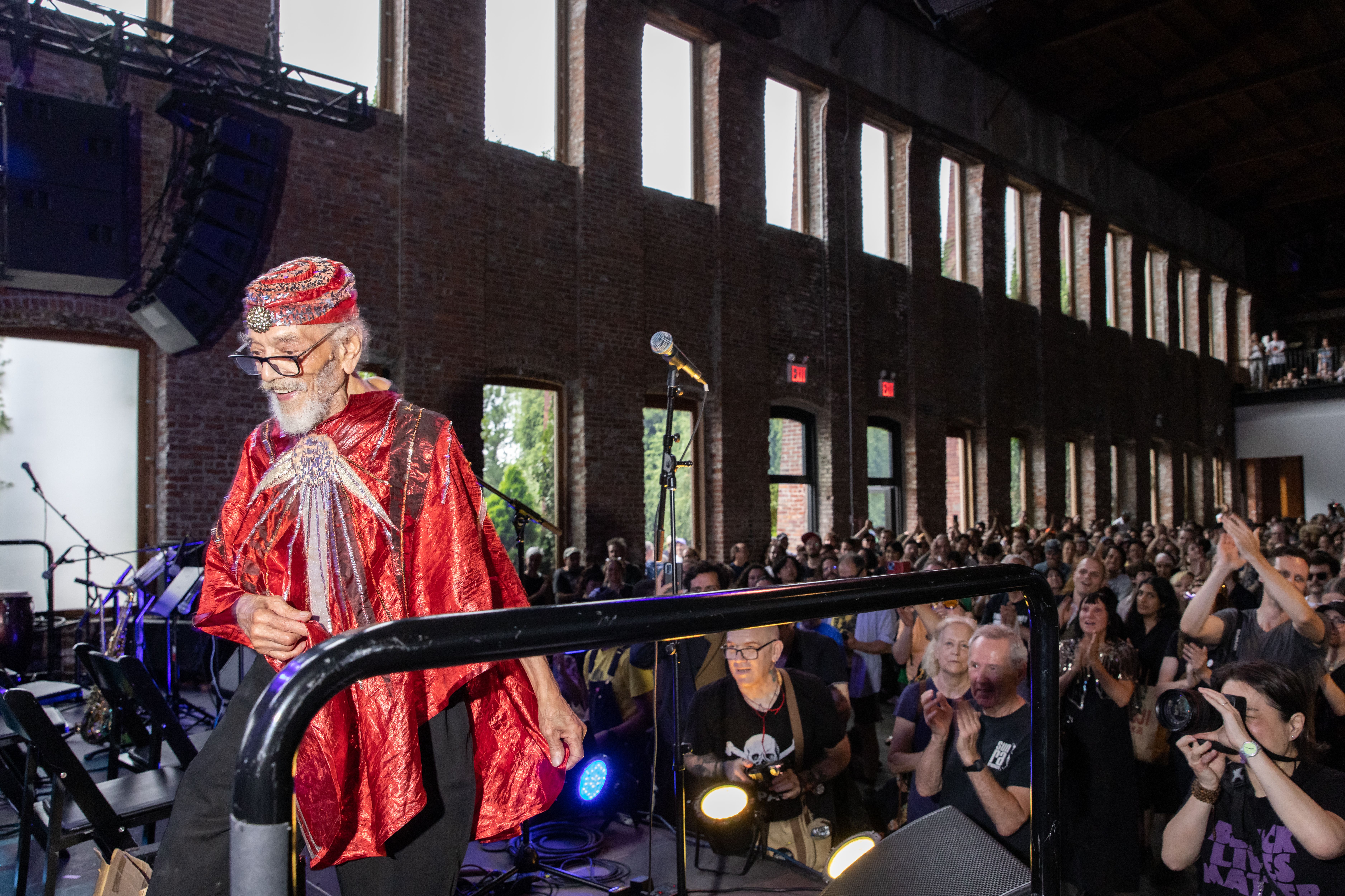 Marshall Allen smiling while performing, holding a microphone and an instrument