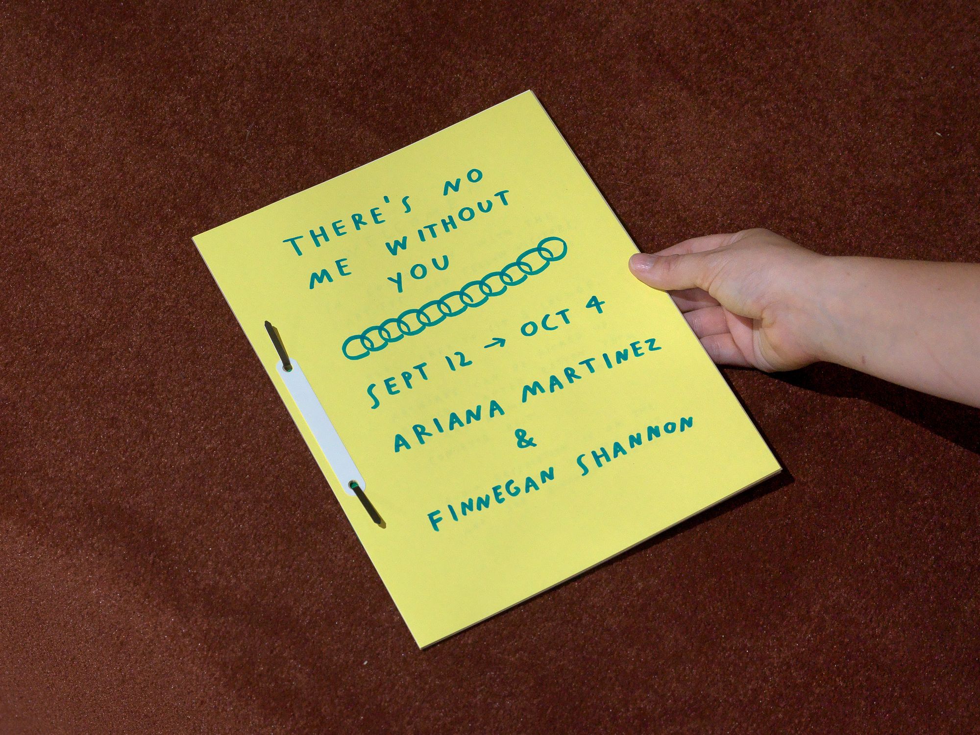 A yellow booklet, with text that reads: "There's no me without you / Sept 12 -> Oct 4 / Ariana Martinez & Finnegan Shannon"