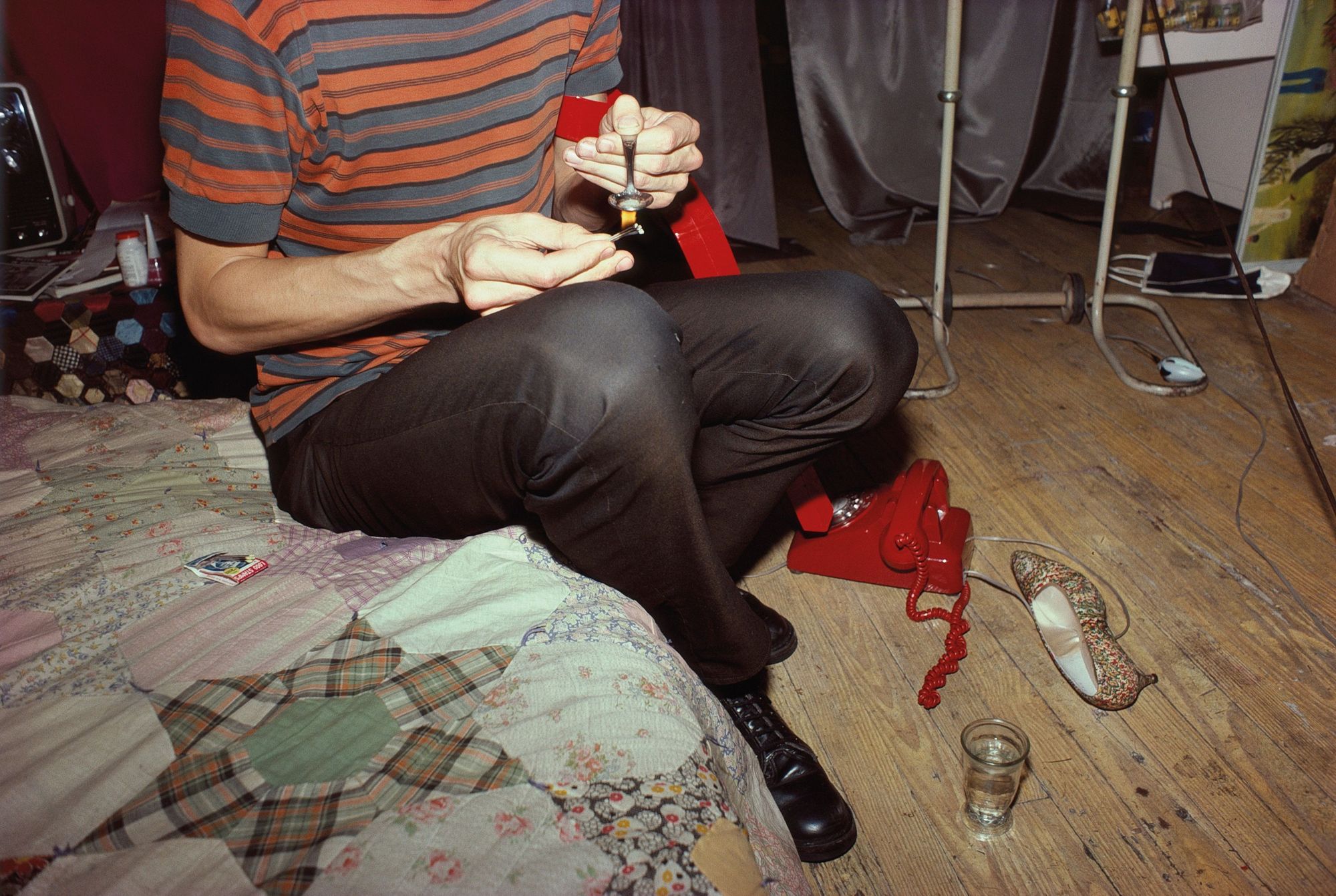 A man heats a spoon or heroin, sitting on a bed
