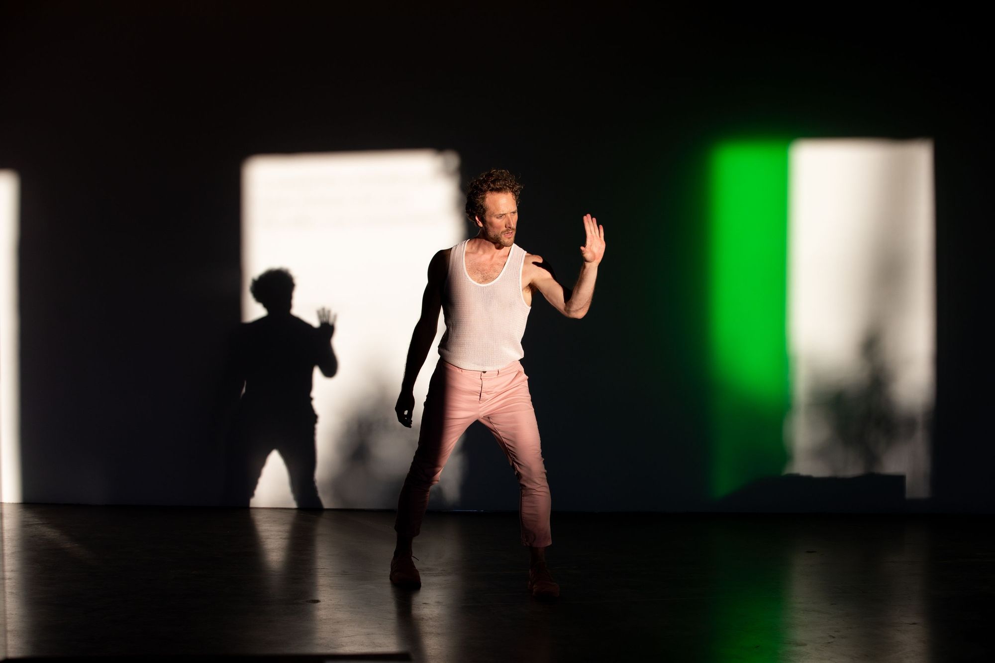 Ryan Kelly dances in CLOCKWORK, with high contrast shadows in the background. 